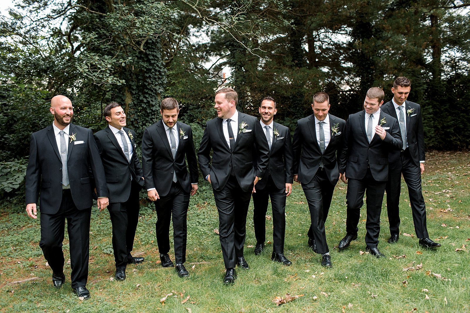 groom walks with groomsmen in black suits on lawn at Aldie Mansion