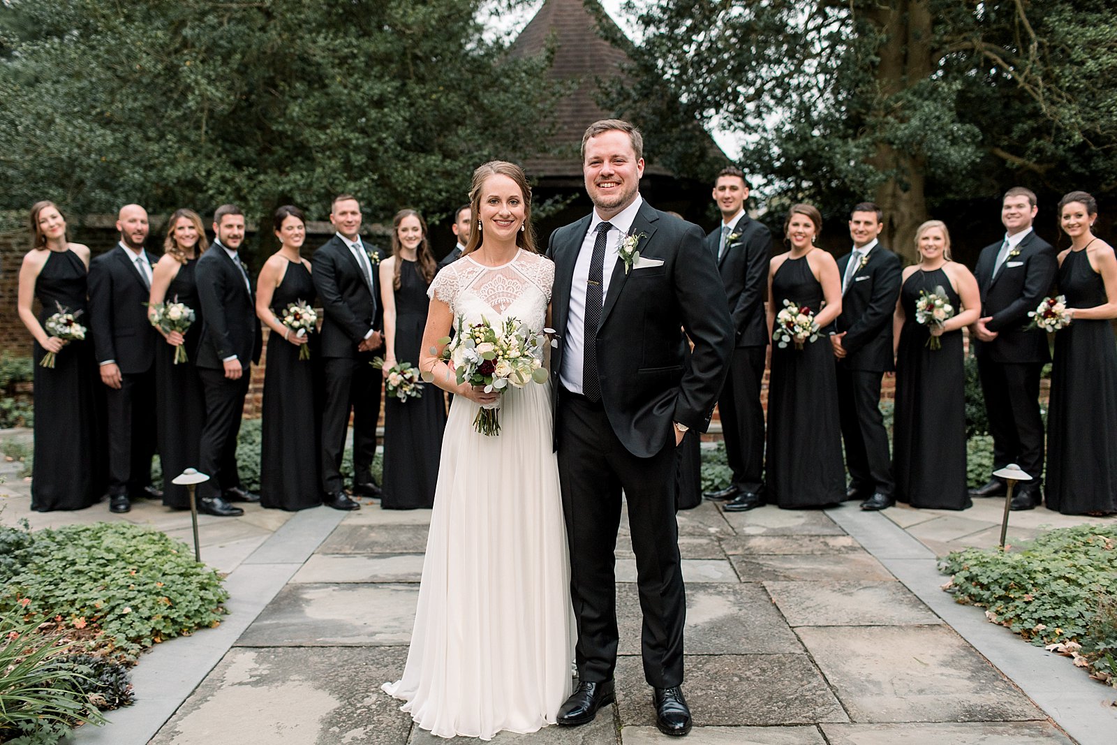 bride and groom stand in front of wedding party in black attire 