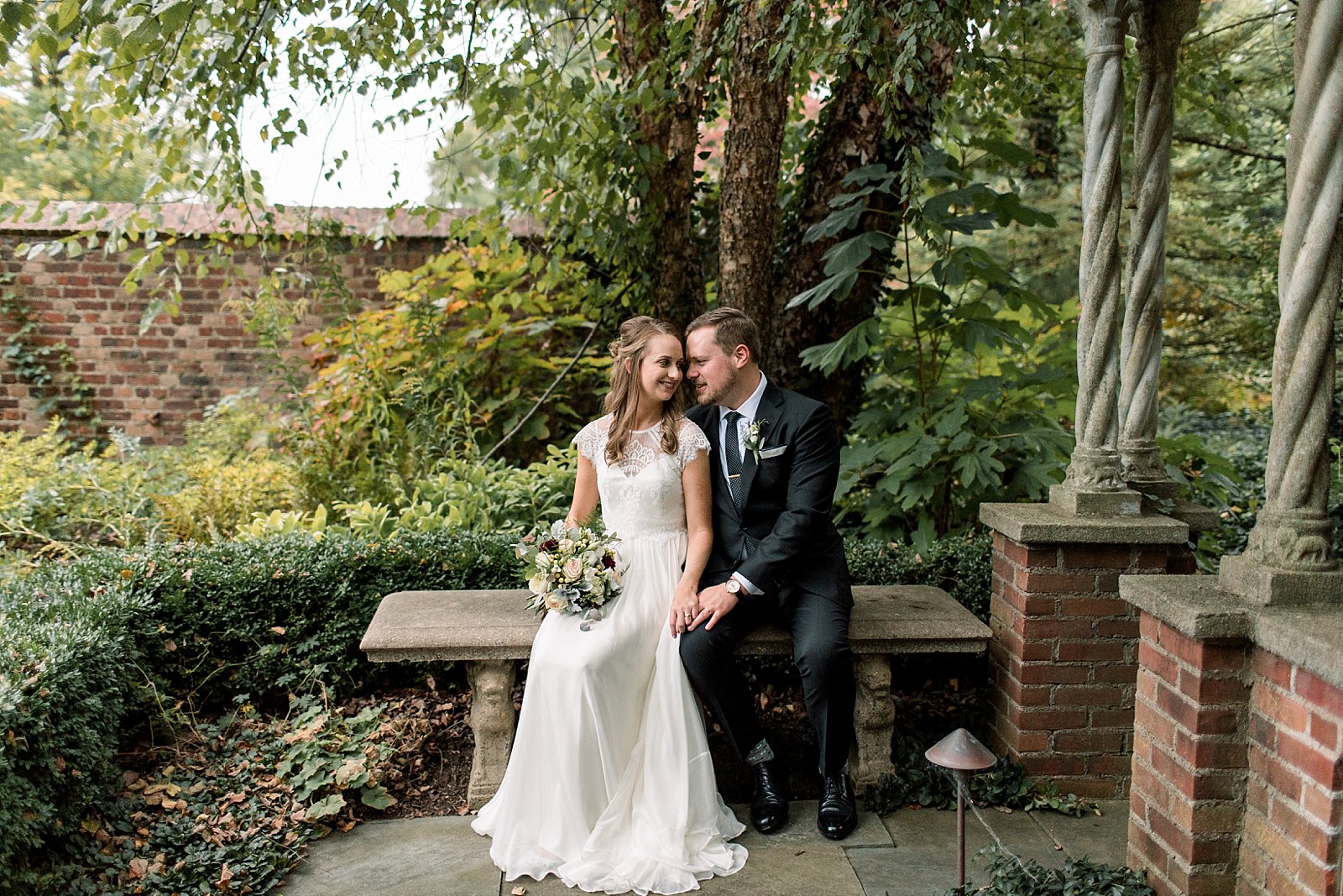 bride and groom sit on stone bench in gardens at Aldie Mansion