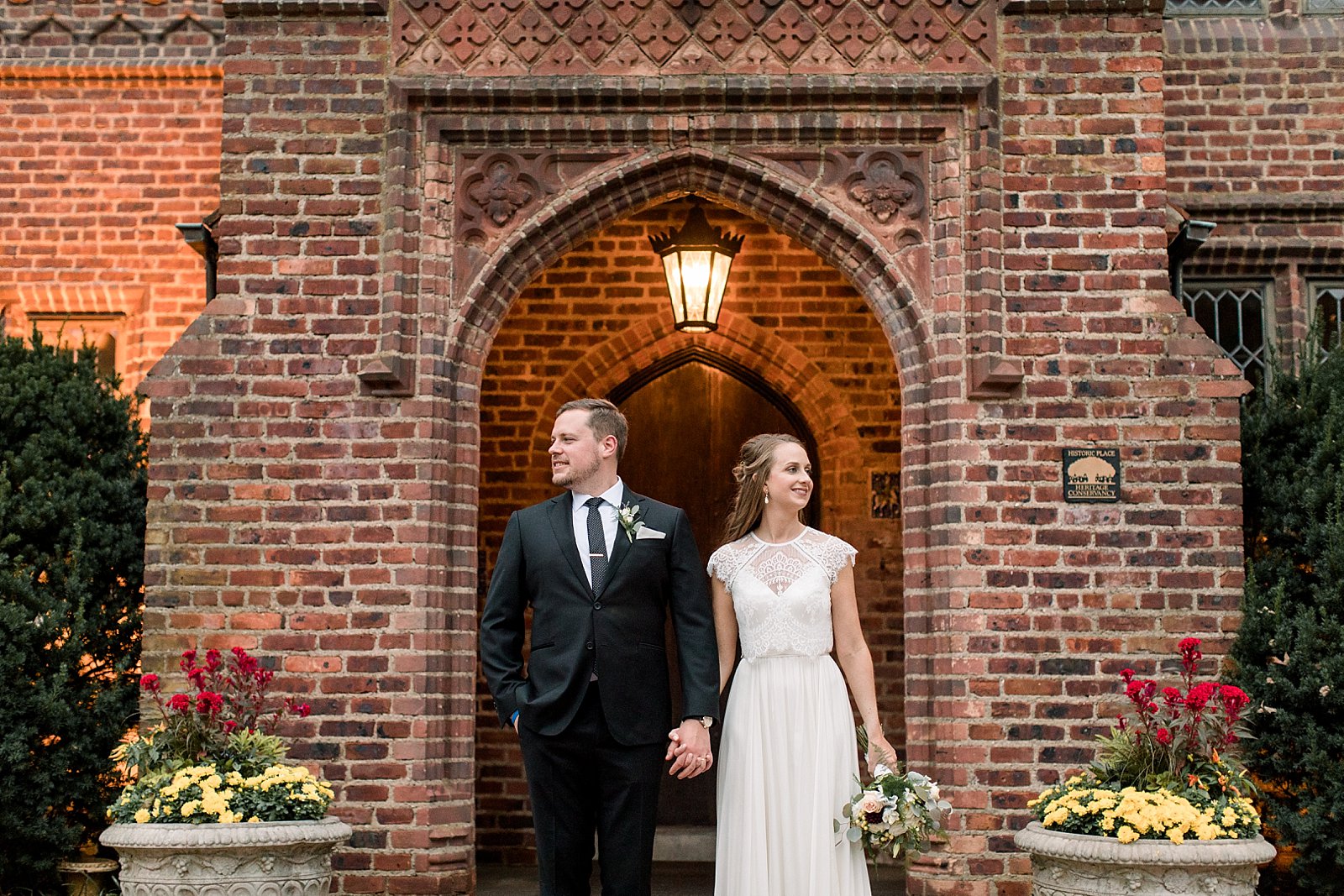 bride and groom hold hands in front of brick wall at Aldie Mansion