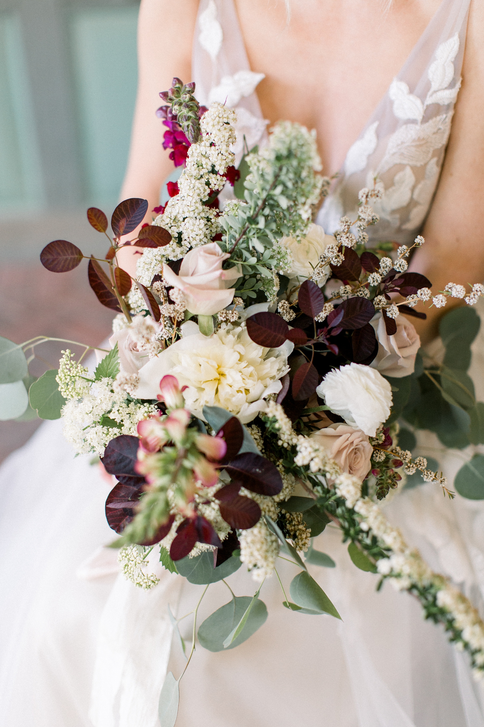 bride holds bouquet of white flowers with green leaves 