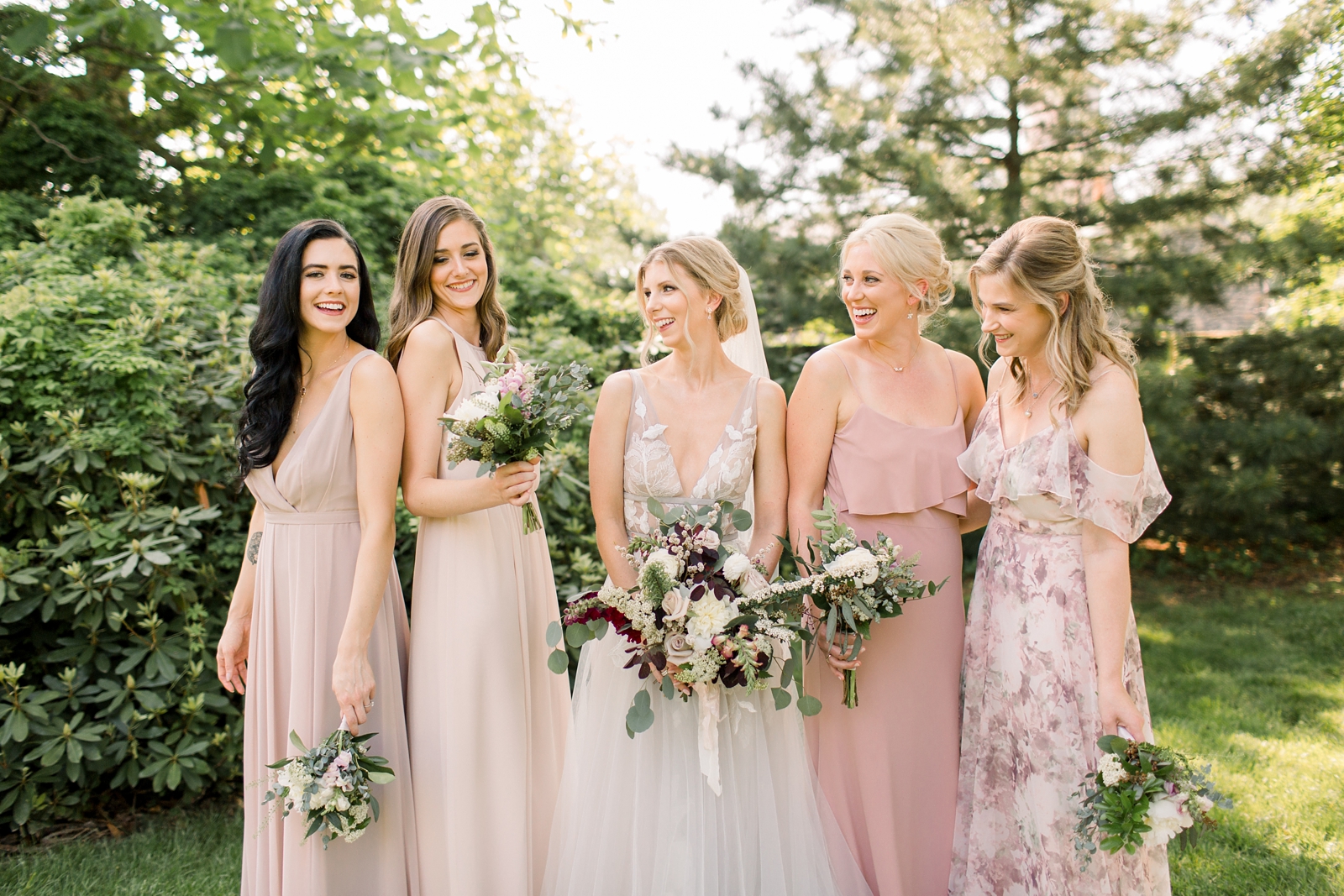 bride stands with bridesmaids in mismatched pink gowns in gardens at The Carriage House at Rockwood Park