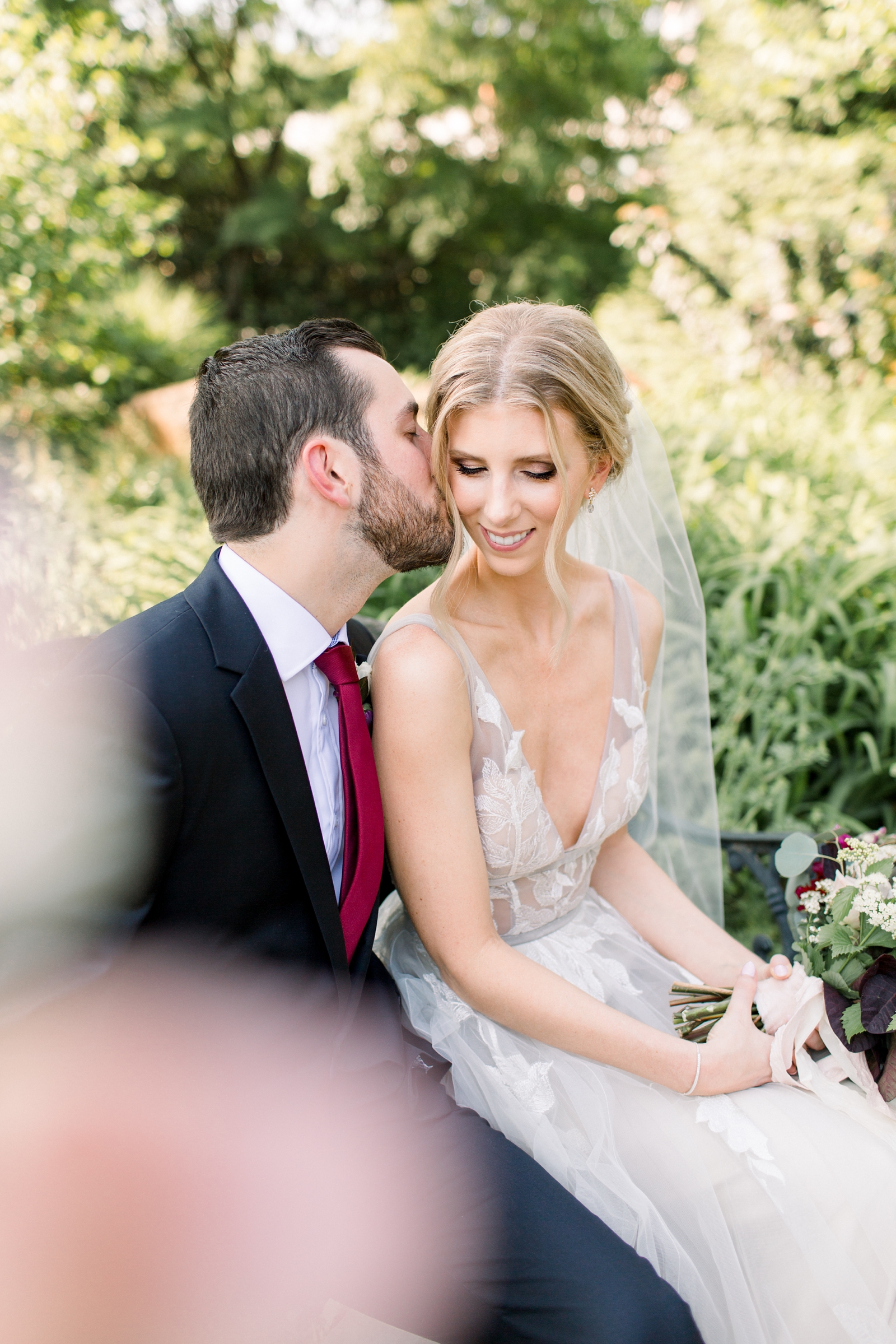 groom kisses bride's cheek sitting in garden at The Carriage House at Rockwood Park