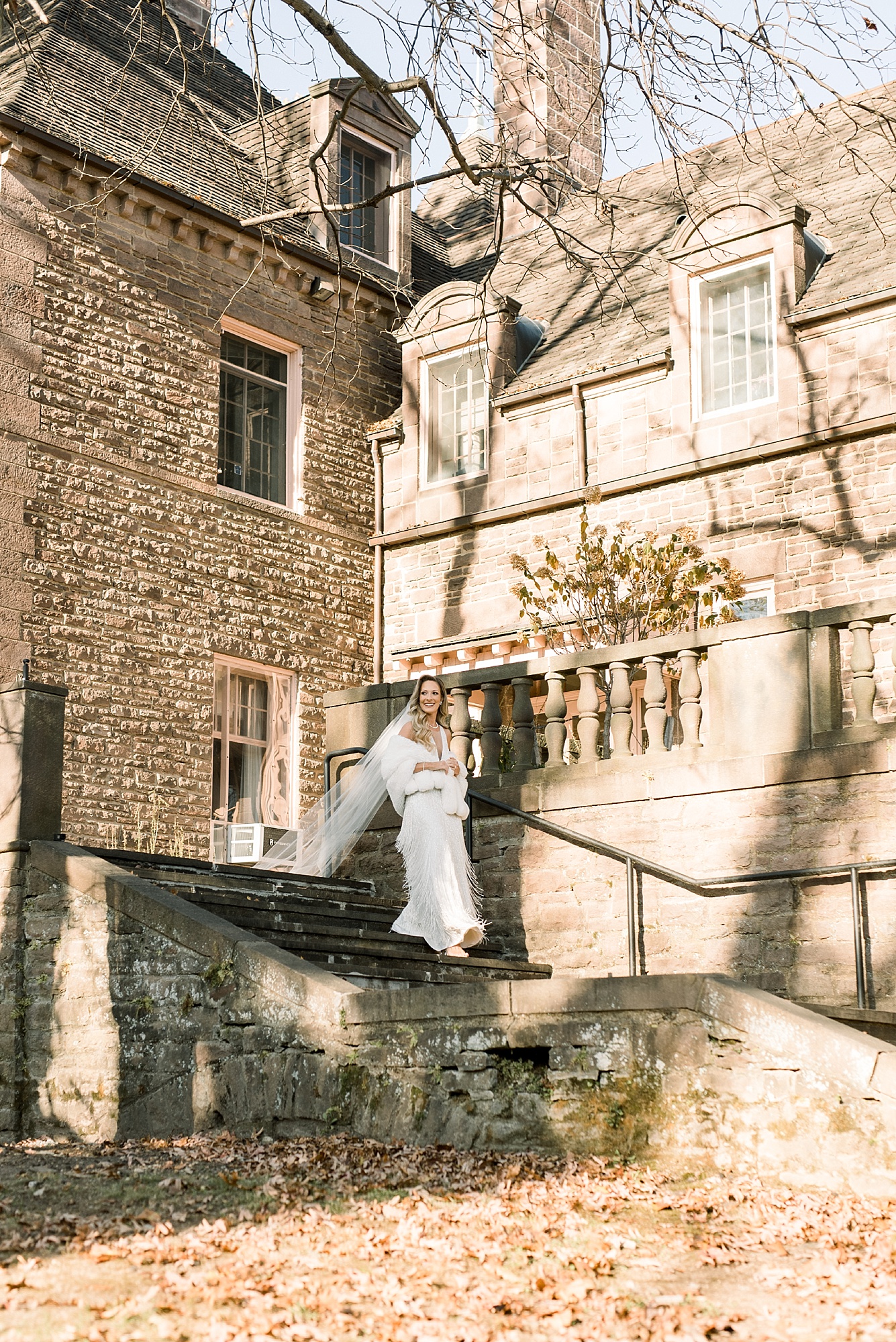 bride walks down steps at Tyler Gardens  with wedding dress with fringe and fur wrap 