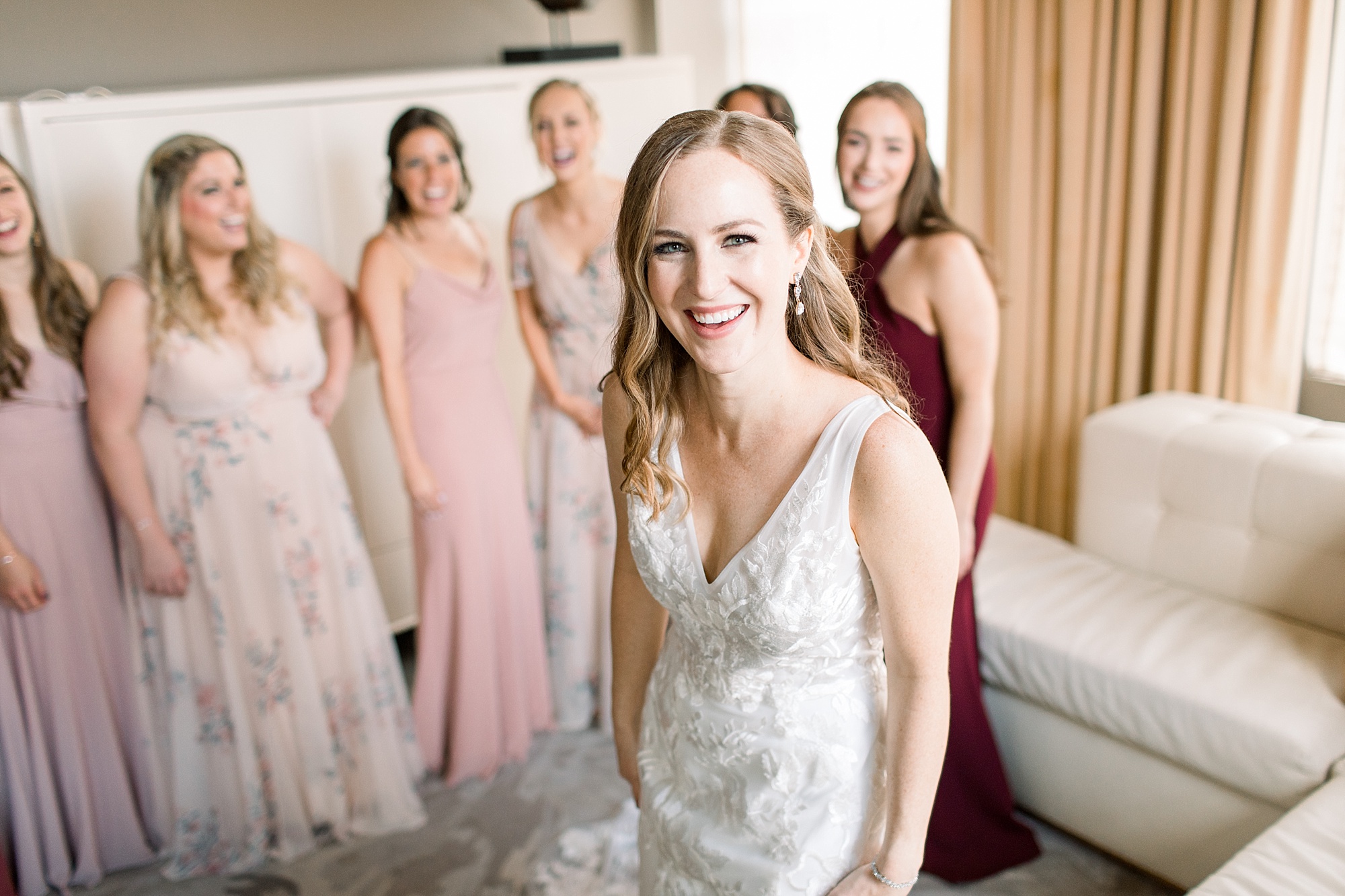 bridesmaids in pink mismatched gowns smiles behind bride 