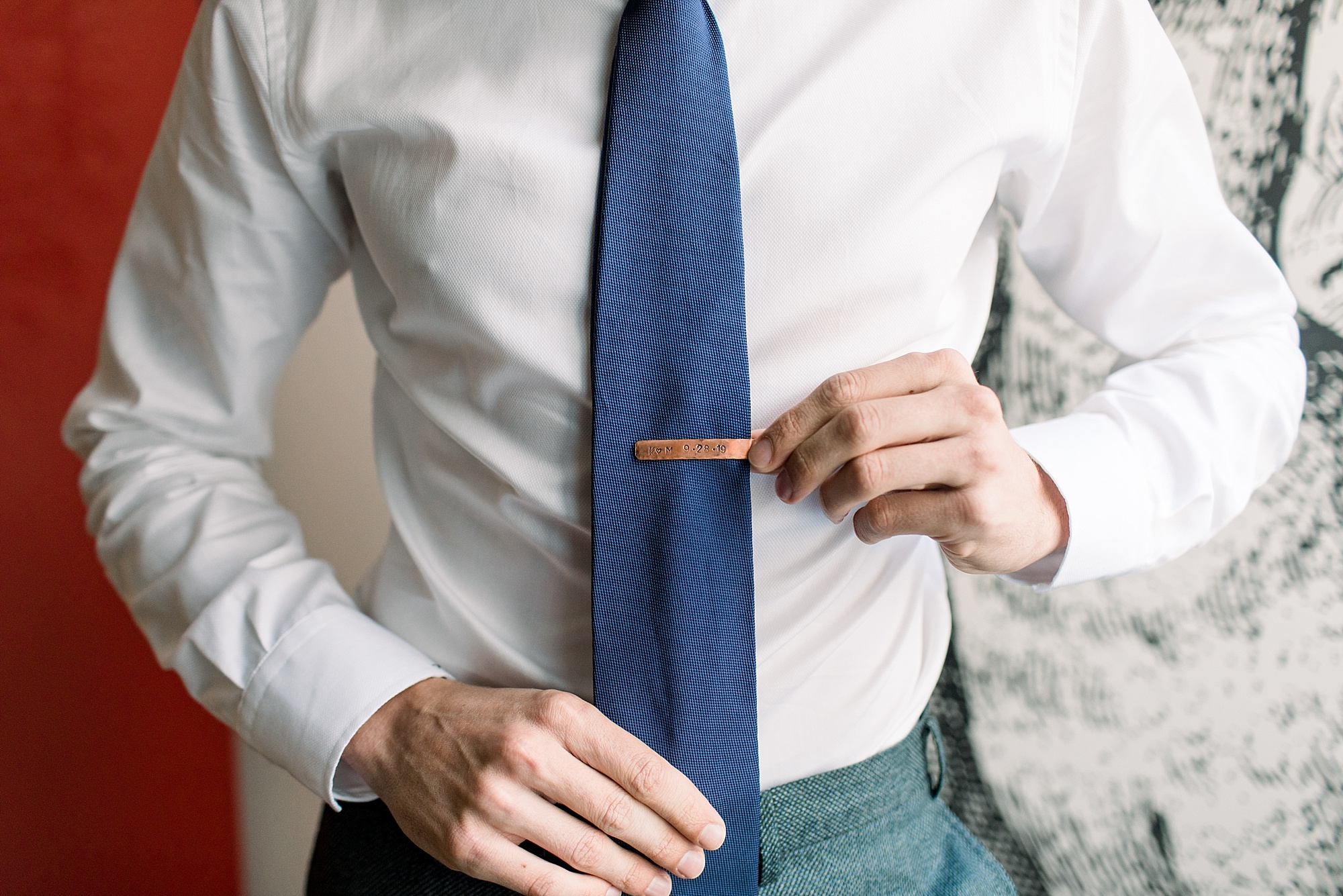 groom places copper tie clip on blue tie 