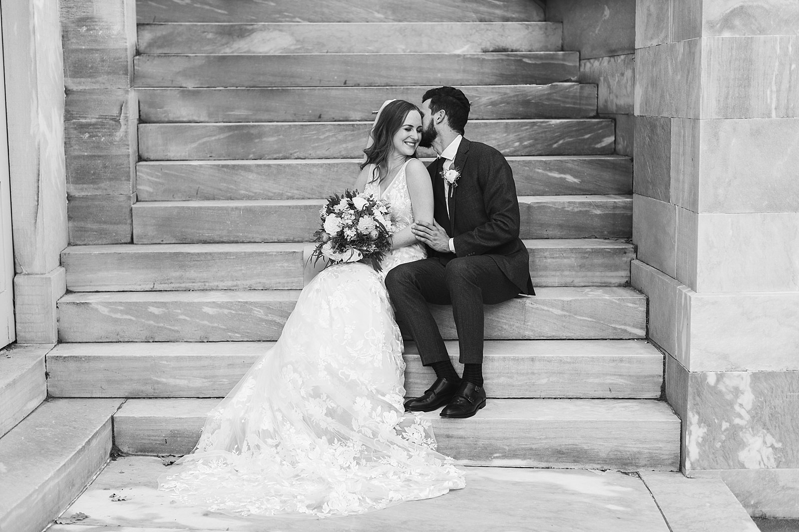 groom sits with bride on steps at the Merchant’s Exchange Building whispering in her ear 