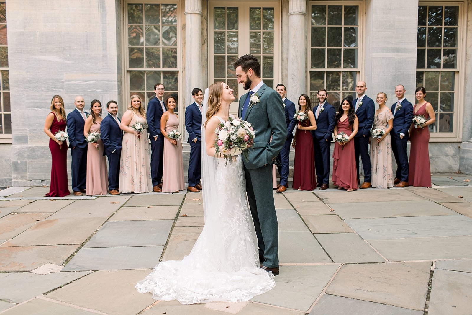 bride and groom stand in front of wedding party in pink and blue attire 