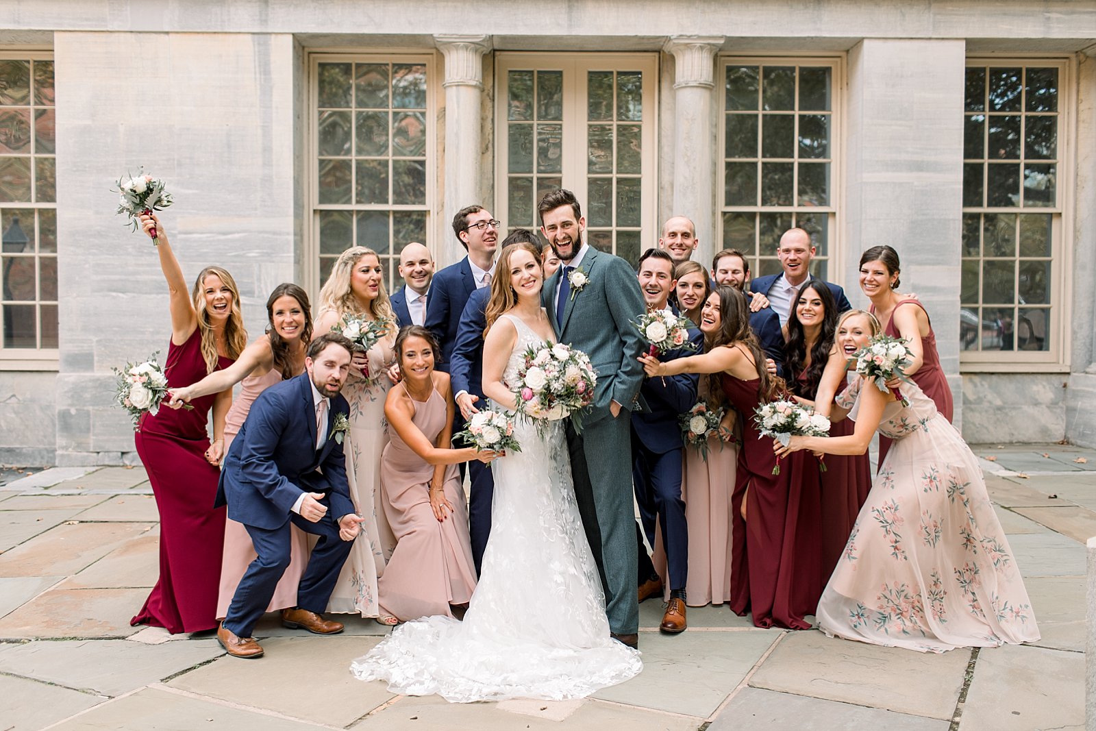 newlyweds hug with bridal party in pink, red, and blue attire 