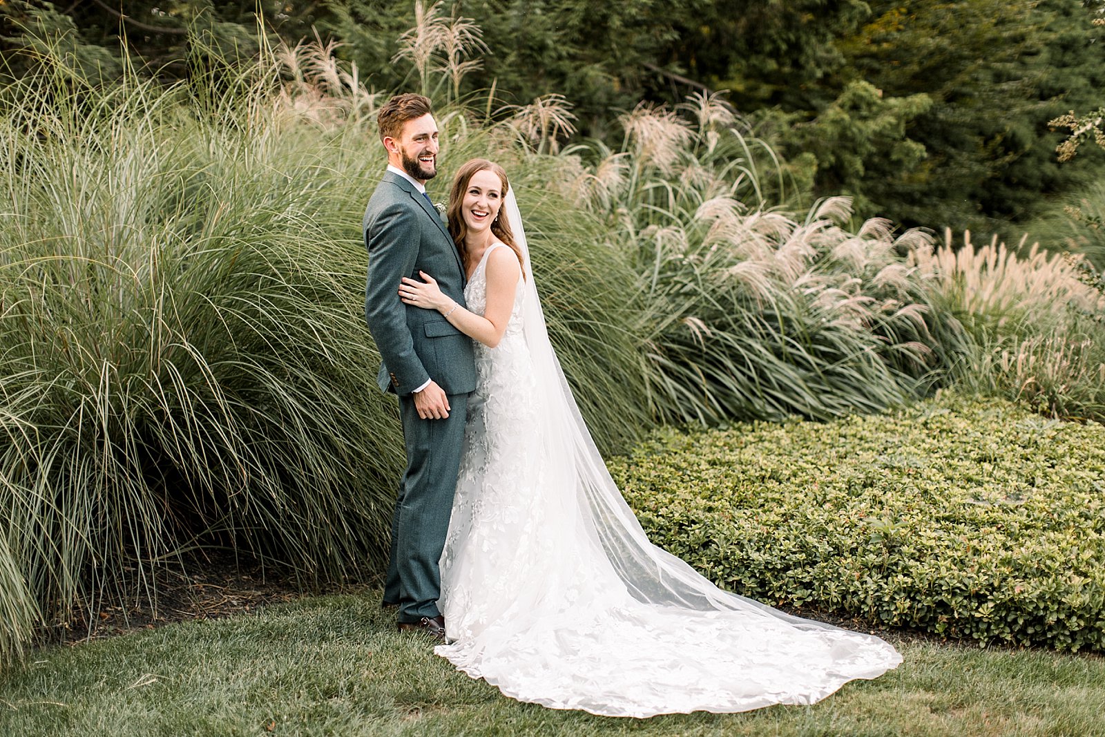 bride hugs groom laughing near tall grass at Knowlton Mansion