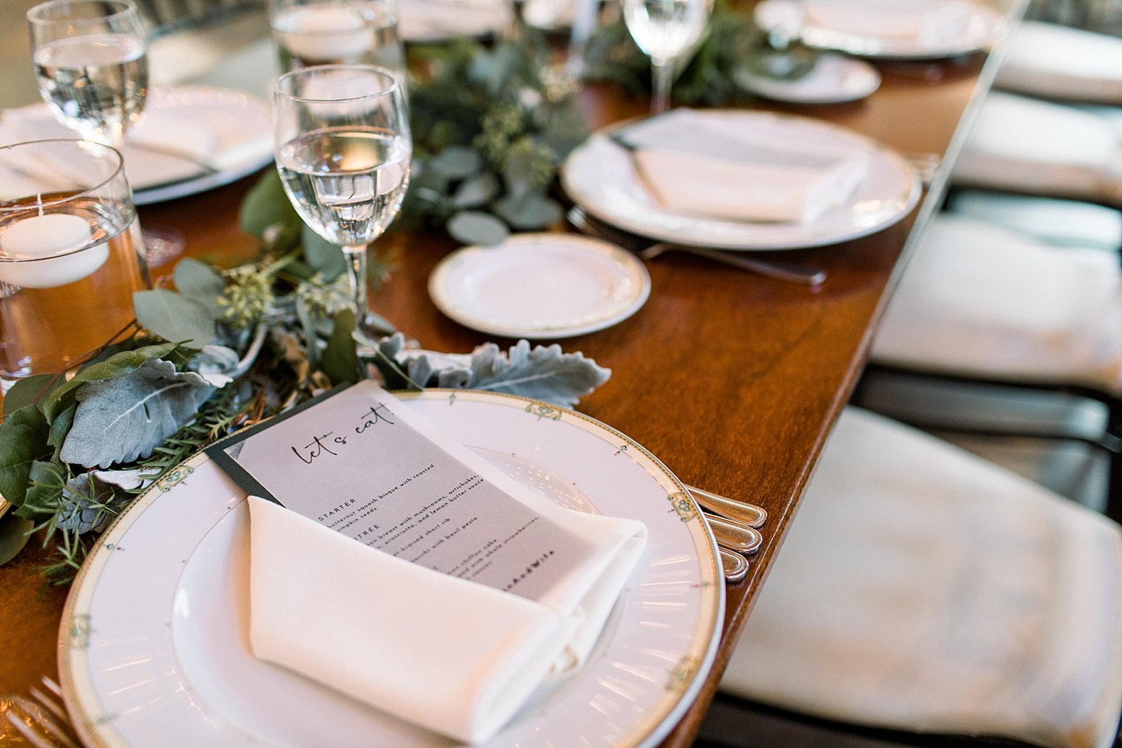 wedding reception place setting with greenery and plates with white and gold rims