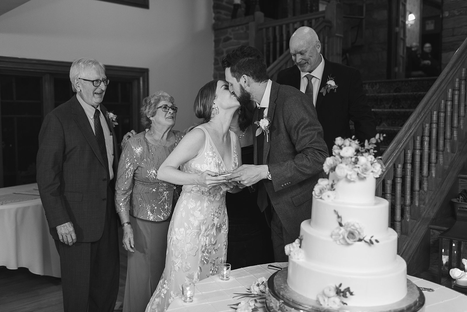 bride and groom kiss by cake with parens behind them during Philly PA wedding reception 