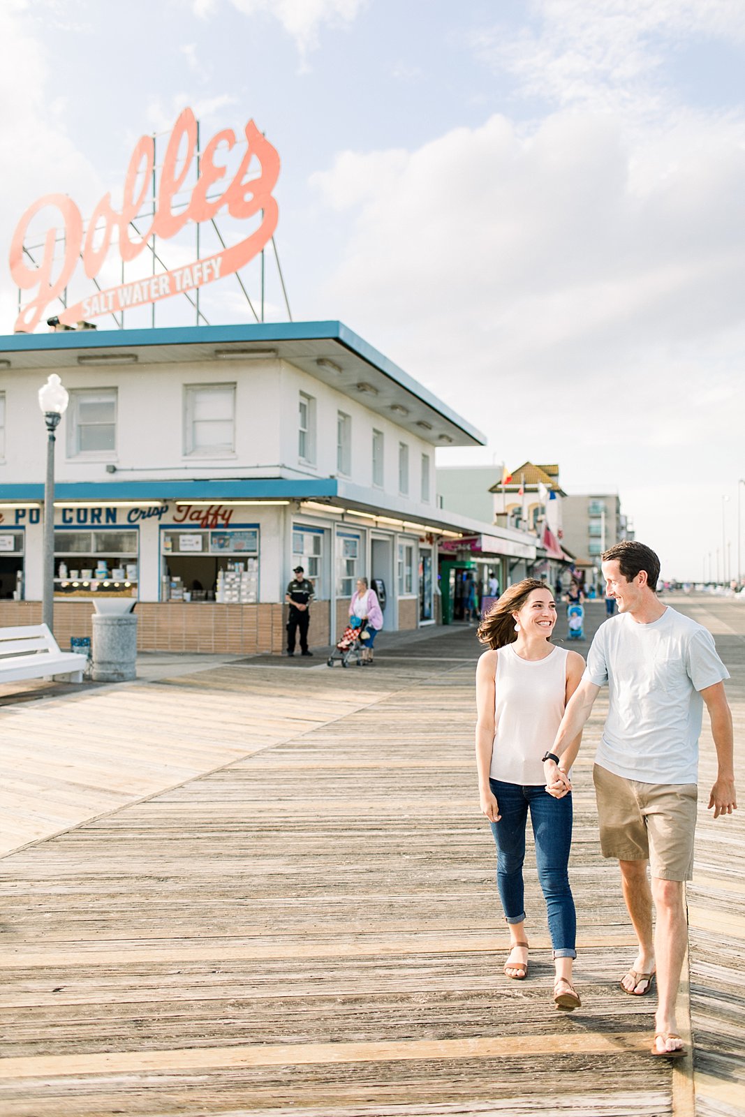 engaged couple holds hands walking down boardwalk at Rehoboth Beach