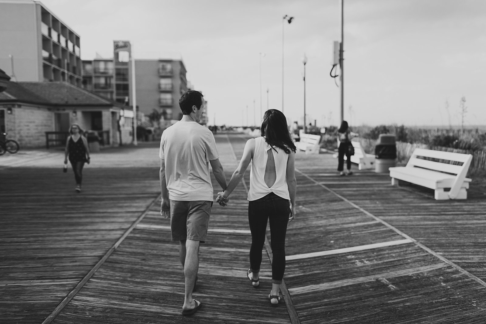 engaged couple holds hands walking on boardwalk 
