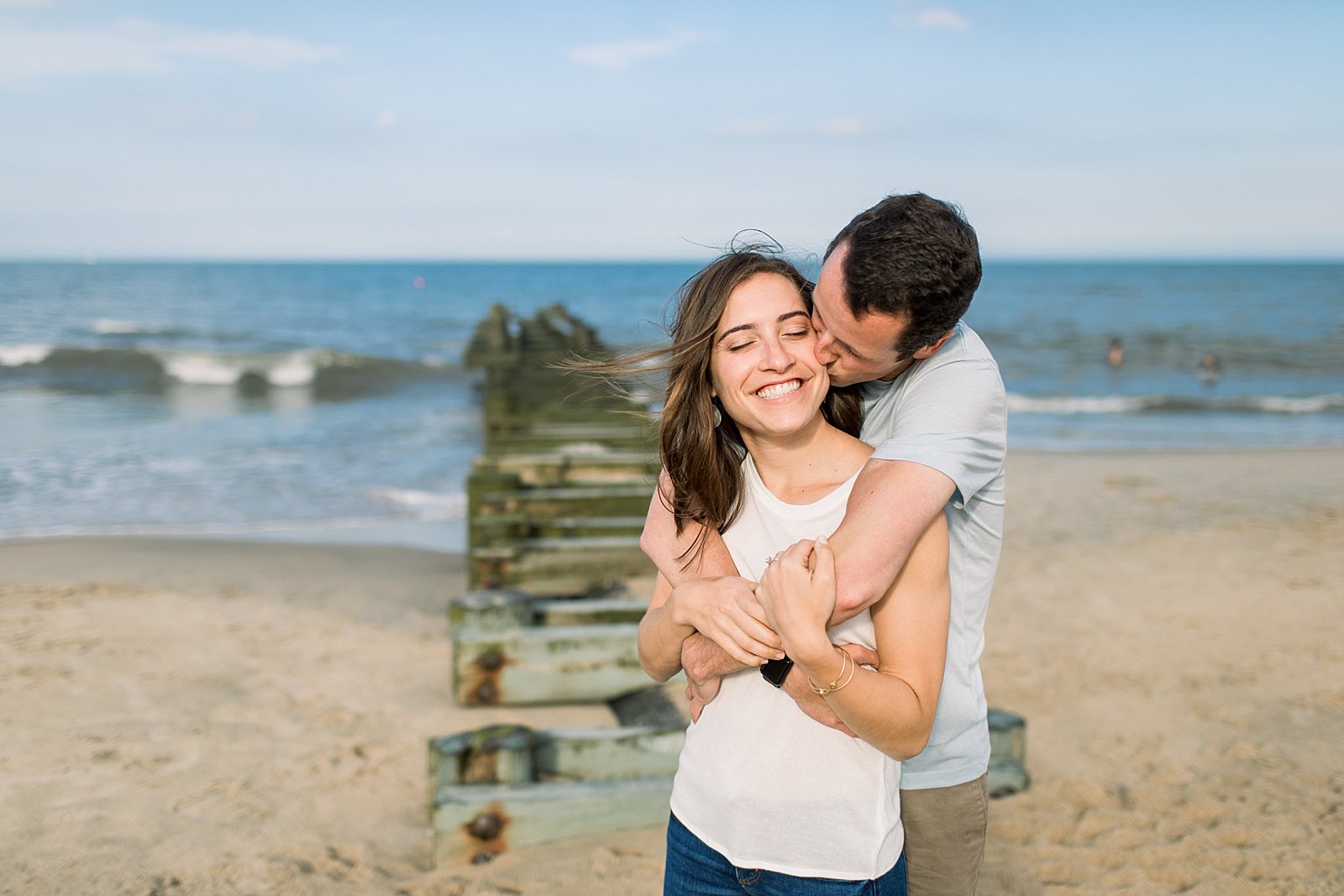 man hugs woman in white tank top around shoulders on Rehoboth Beach