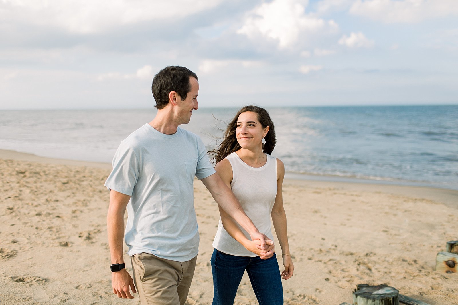 engaged couple holds hands walking down beach during Rehoboth Beach engagement session 