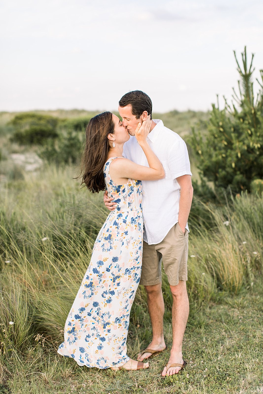 man kisses woman in white floral dress on beach during engagement photos 