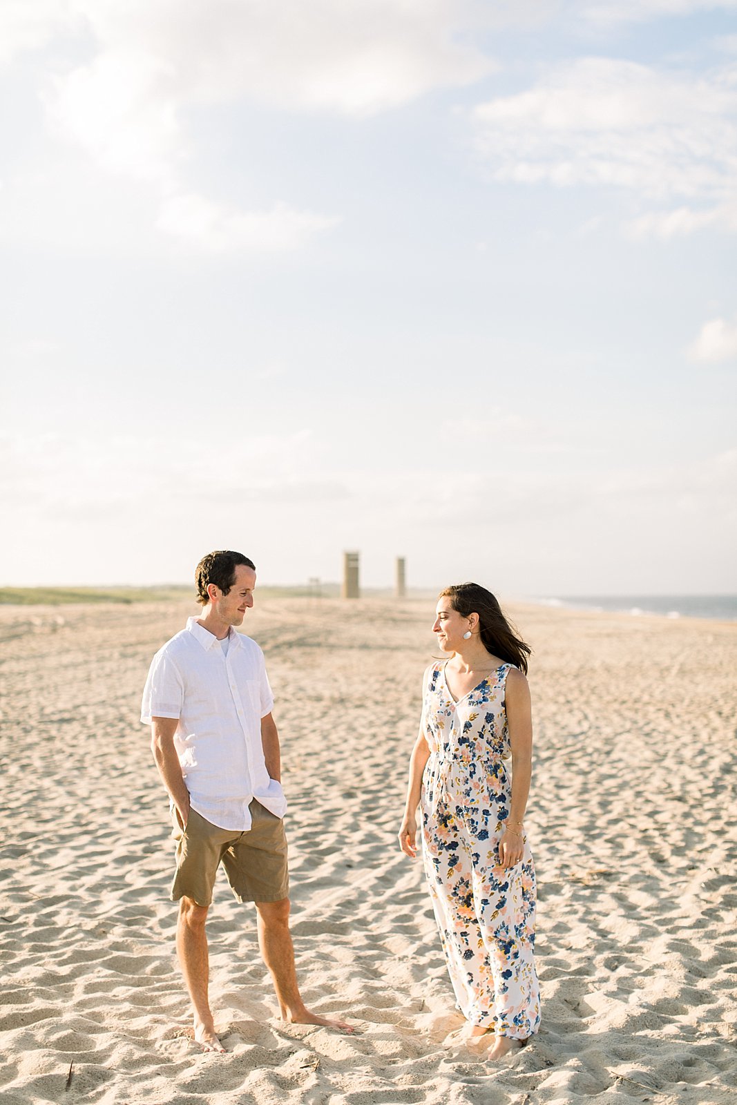 engaged couple walks down beach looking at each other 