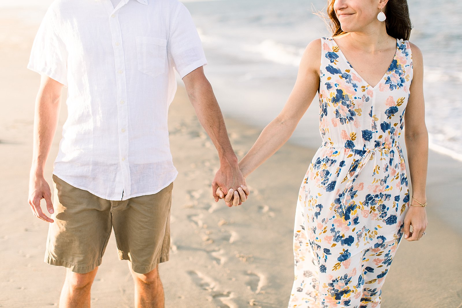 engaged couple holds hands on Rehoboth Beach near ocean 