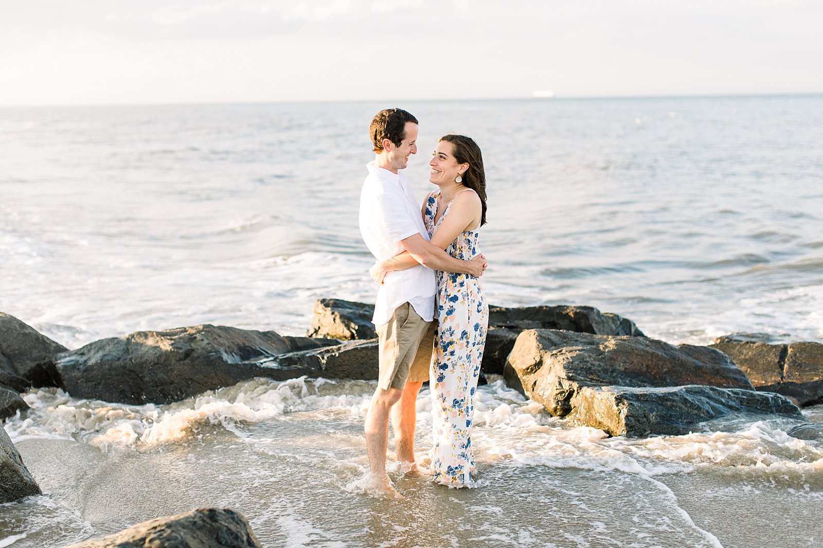 engaged couple hugs on rocks at Rehoboth Beach