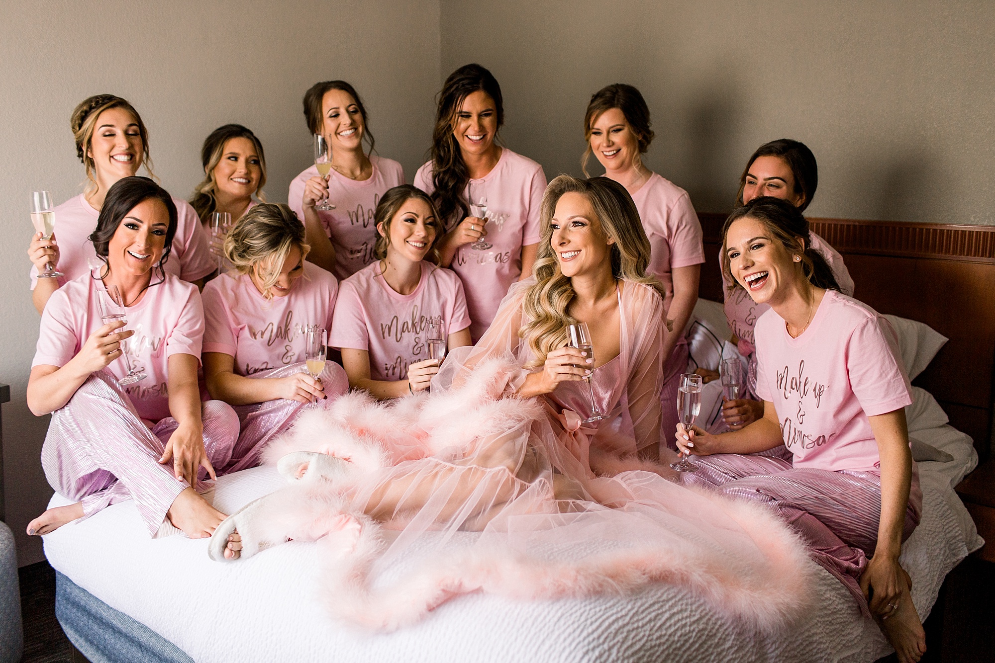 bride in fluffy pink robe sits with bridesmaids in custom pajamas on bed