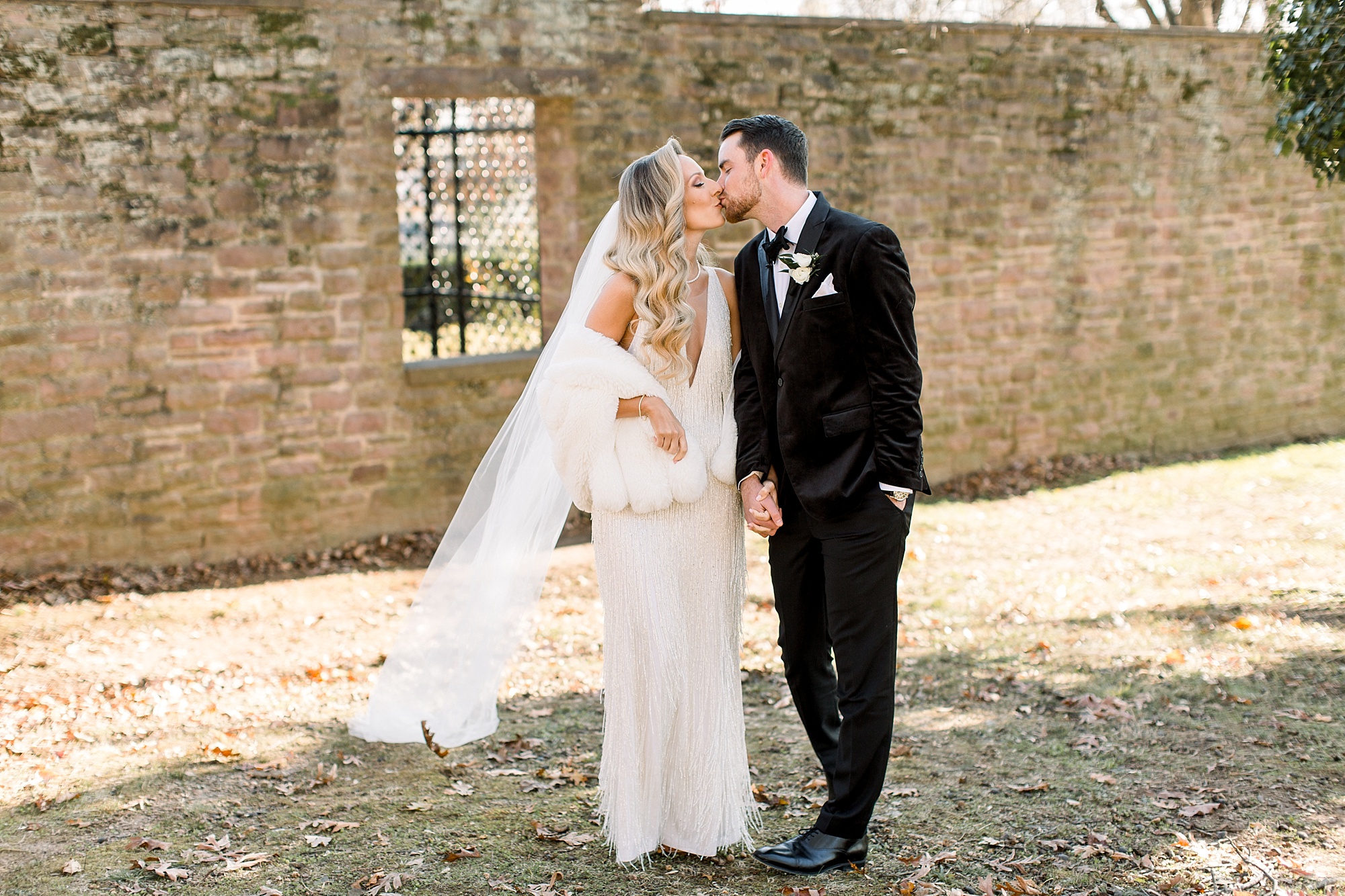 bride with fringe on dress and fur wrap and groom kiss in courtyard at Tyler Gardens 