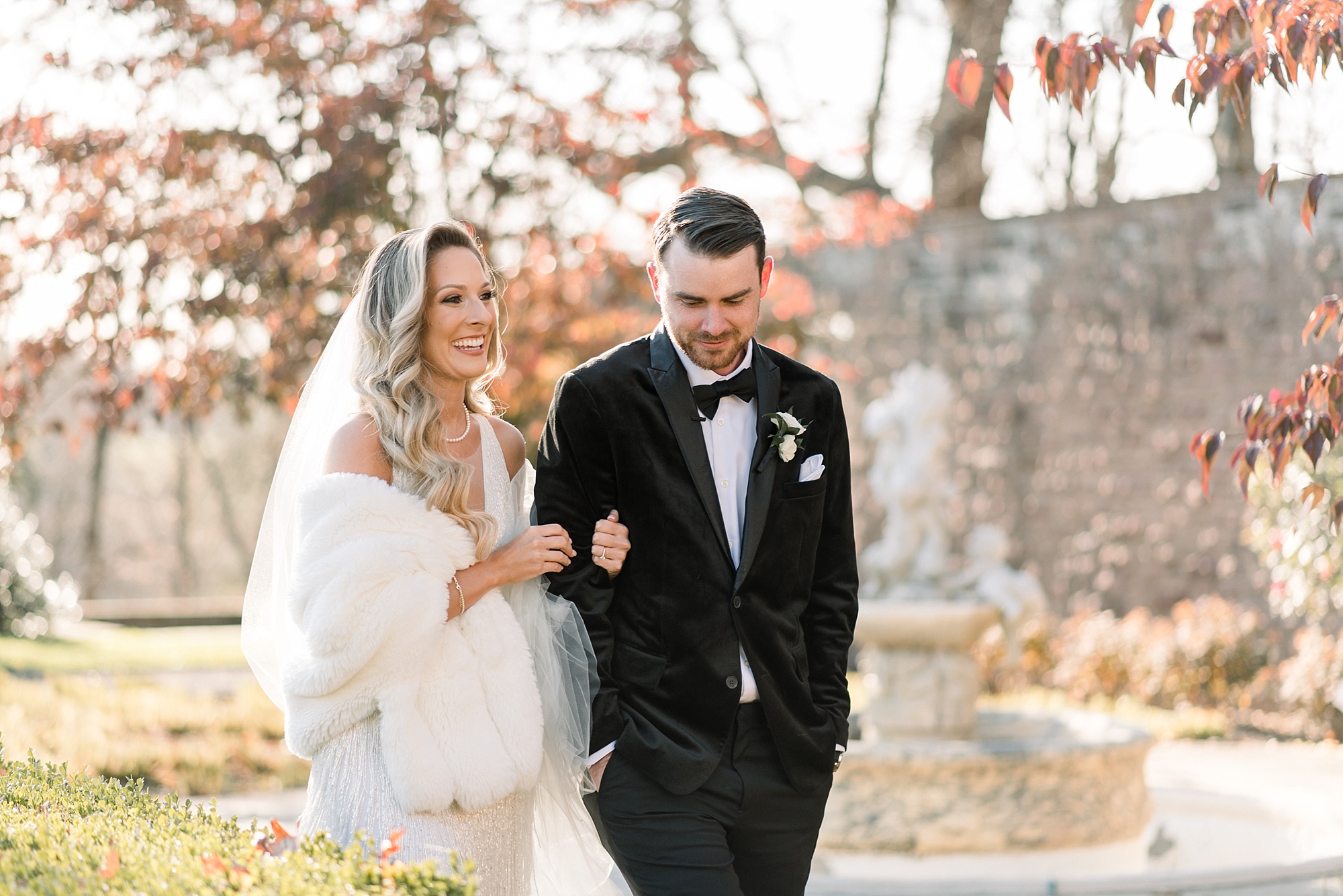 bride in fringe dress with fur wrap walks holding groom's arm 