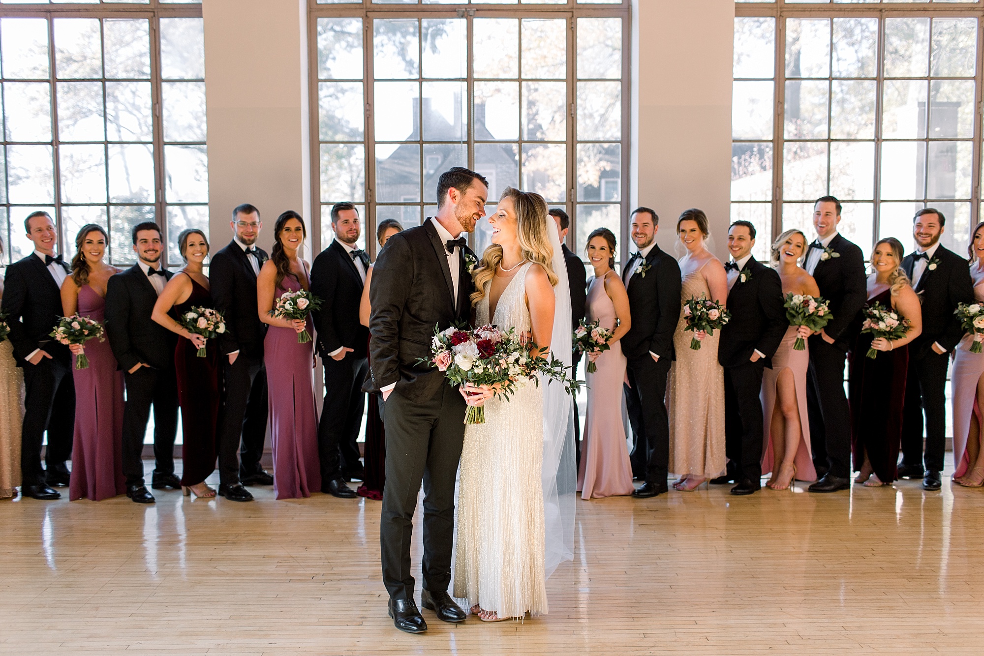 bride and groom lean to kiss in ballroom with wedding party behind them at Tyler Gardens