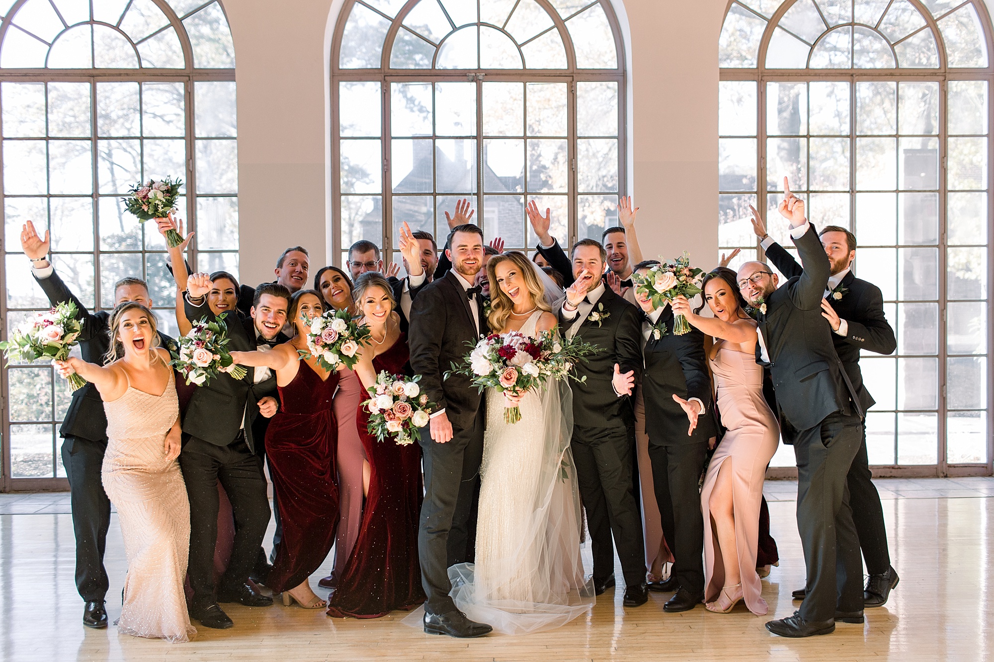 bride and groom stand cheering with bridesmaids in pink dresses and groomsmen in suits 