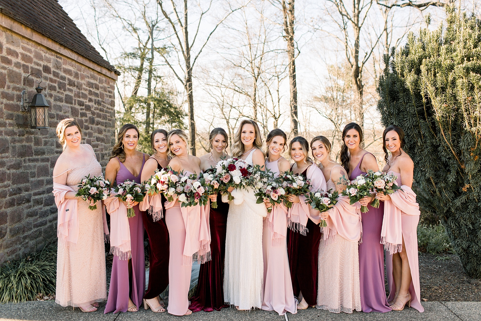 bride poses with bridesmaids in mismatched pink and purple dresses with red and white bouquets 