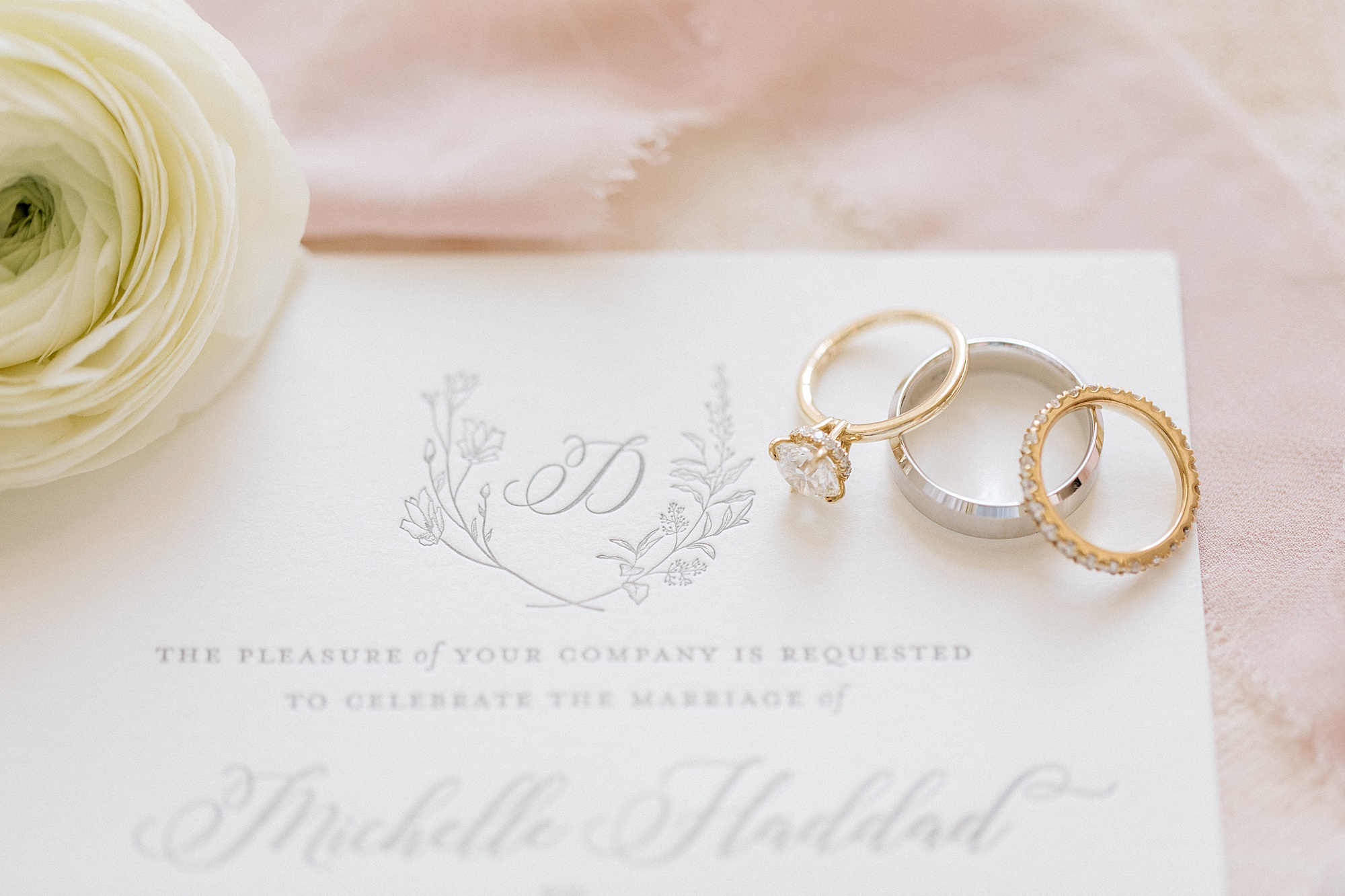 two gold wedding bands lay on silver band on invitation suite with grey embossing 