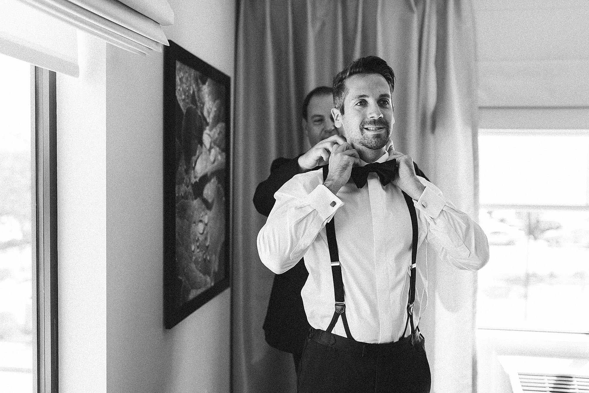 groomsman helps groom with tie and suspenders 