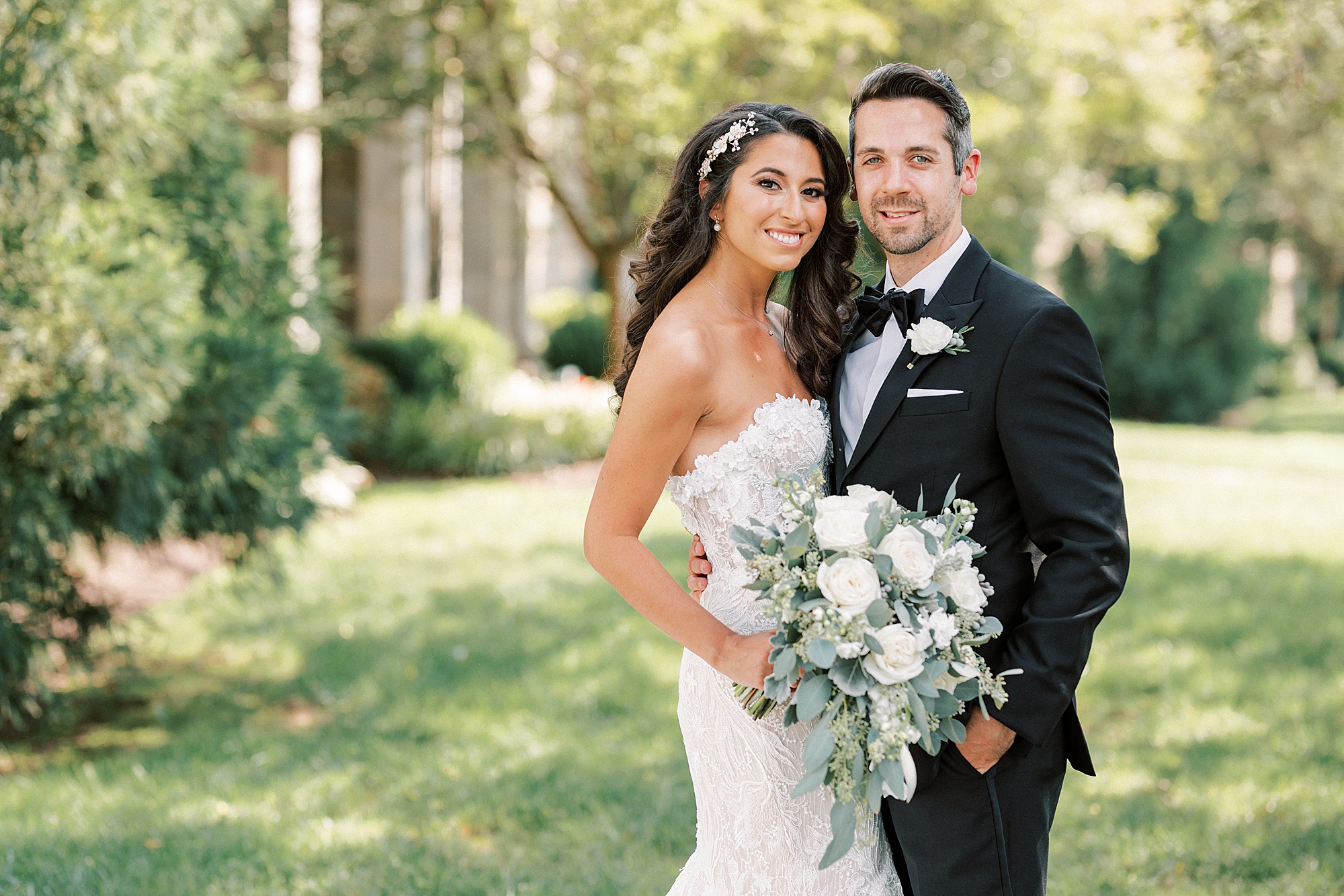 bride cuddles up to groom holding bouquet of white roses 