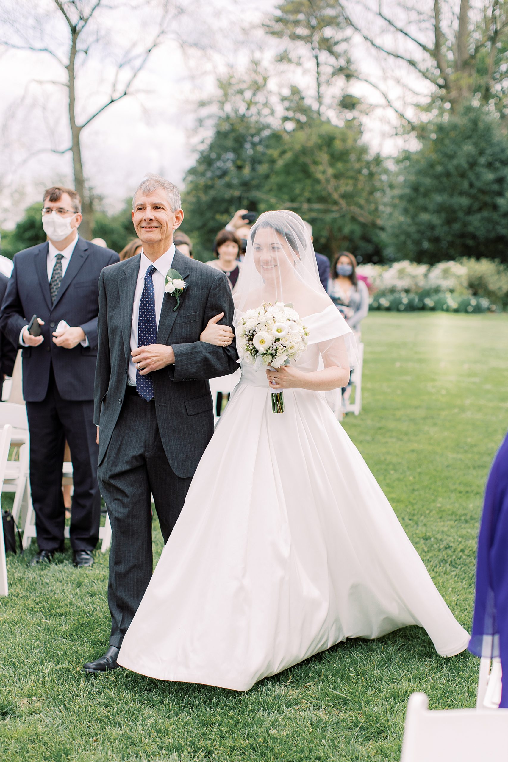 bride holds father's arm walking down aisle for outdoor lawn ceremony at Bellevue Hall