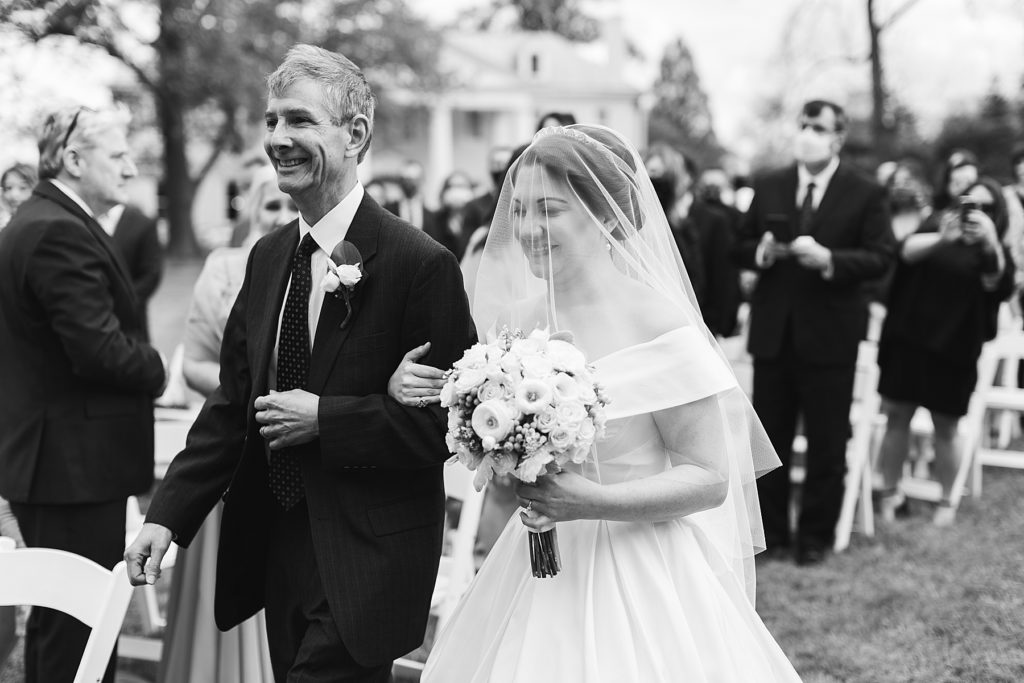 black and white portrait of bride walking down aisle with father at Bellevue Hall