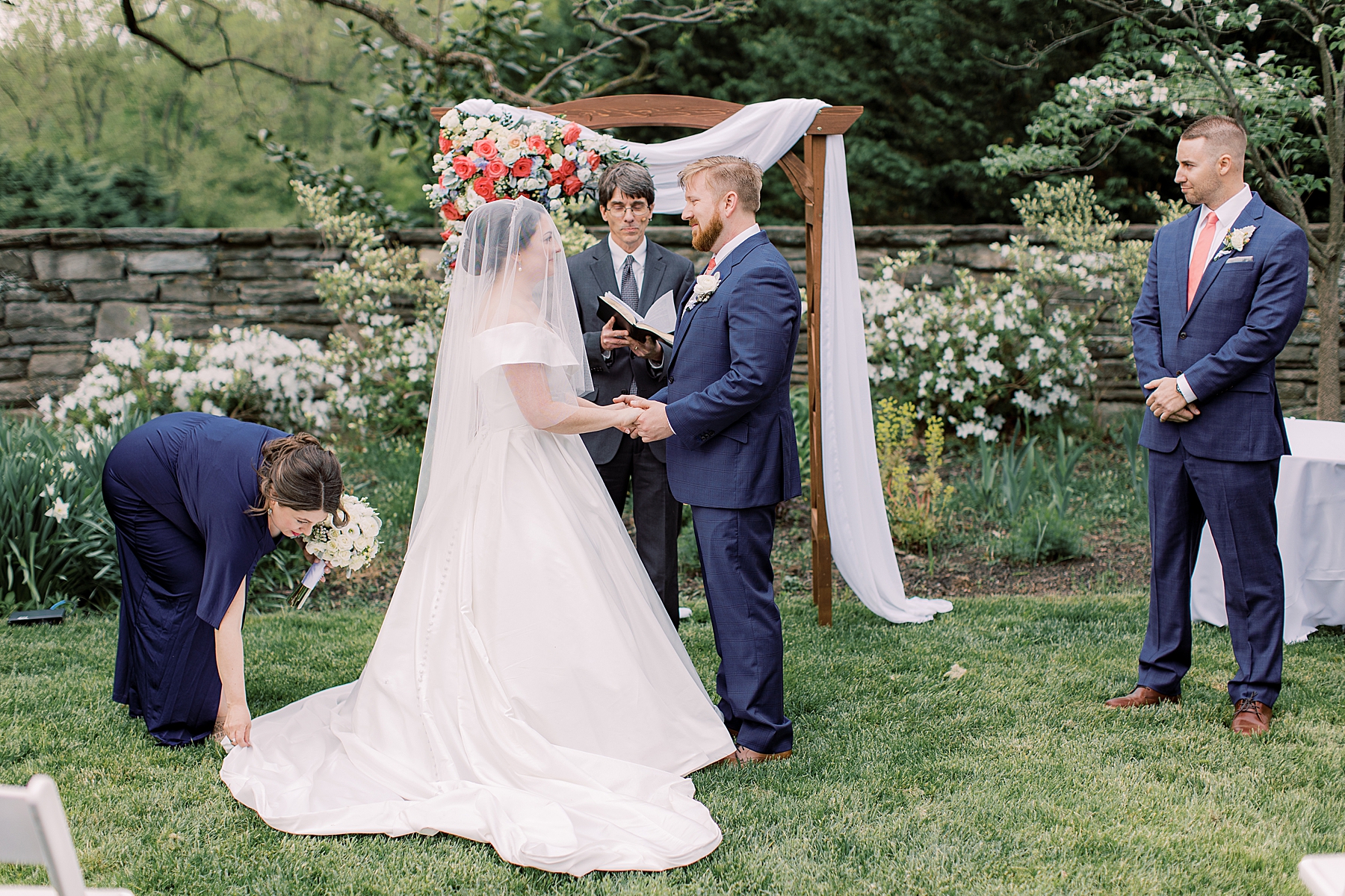 couple exchanges vows by arbor on lawn at Bellevue Hall