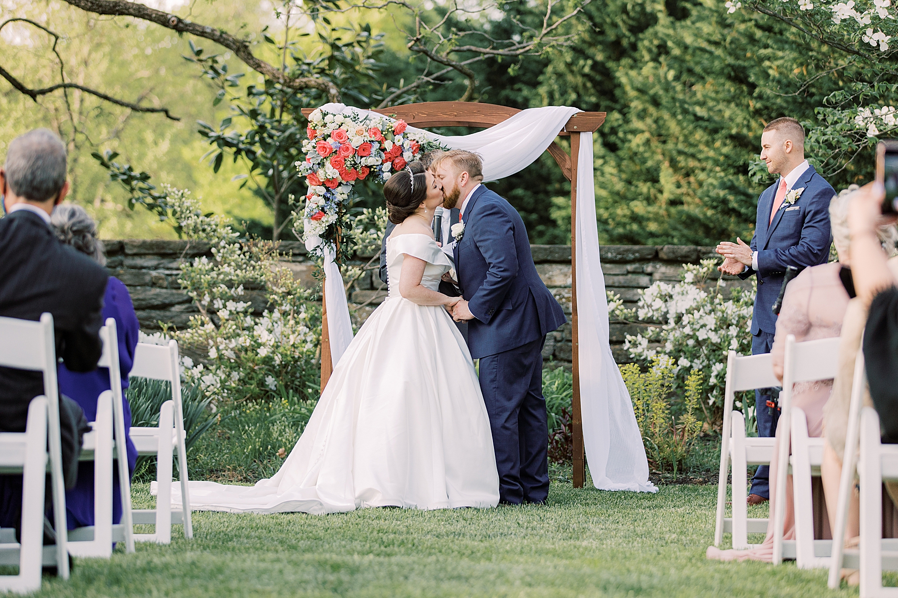 newlyweds kiss in front of wooden arbor at Bellevue Hall