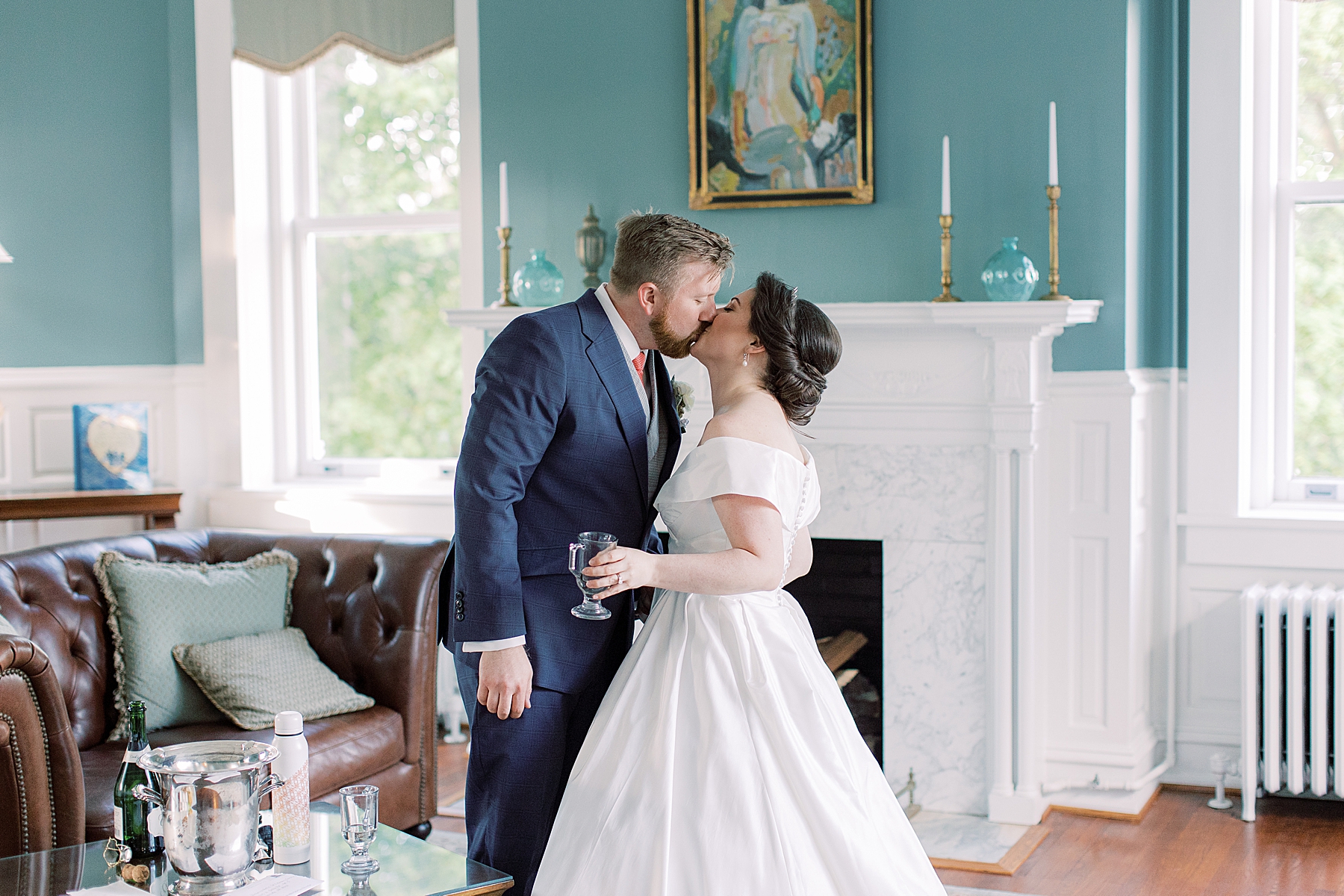 newlyweds kiss by fireplace and teal wall at Bellevue Hall