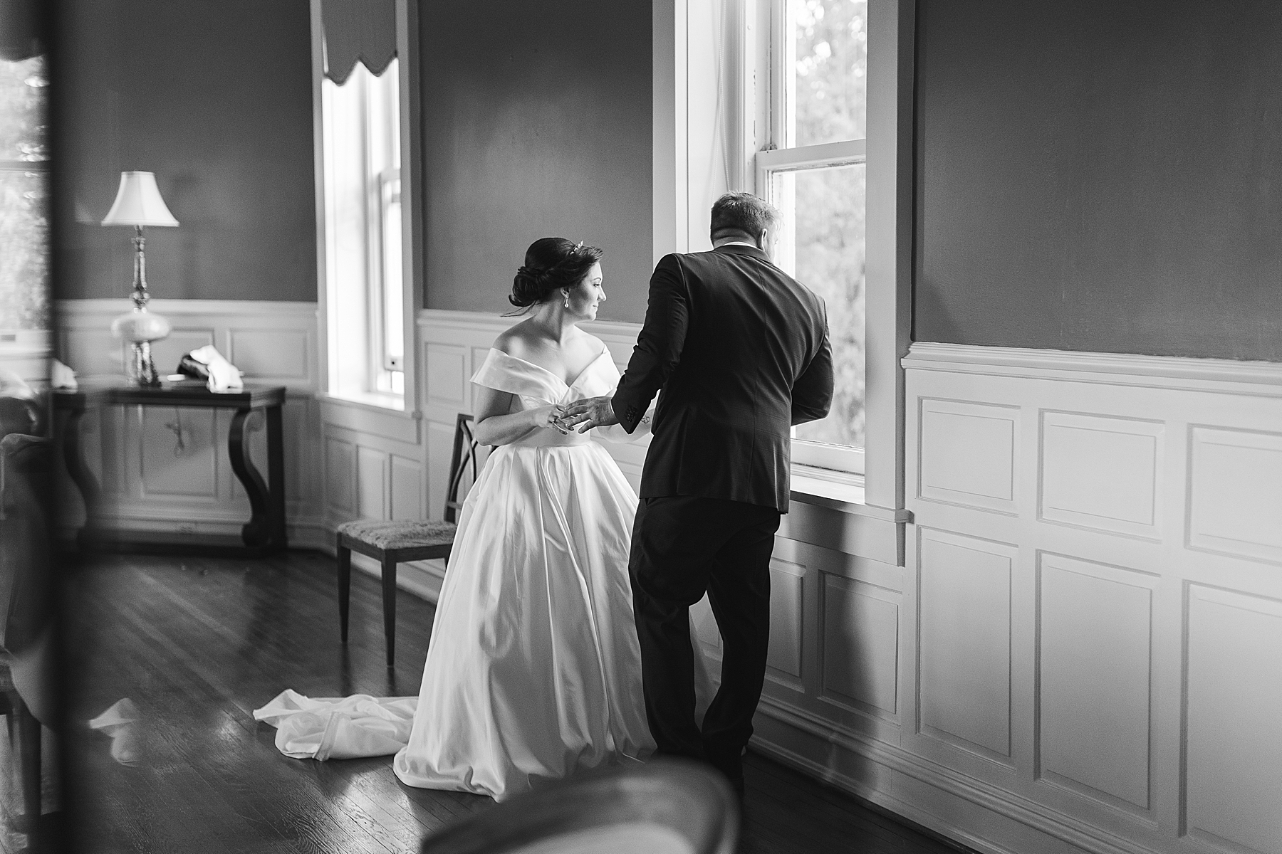 bride and groom look out window at guests on lawn at Bellevue Hall