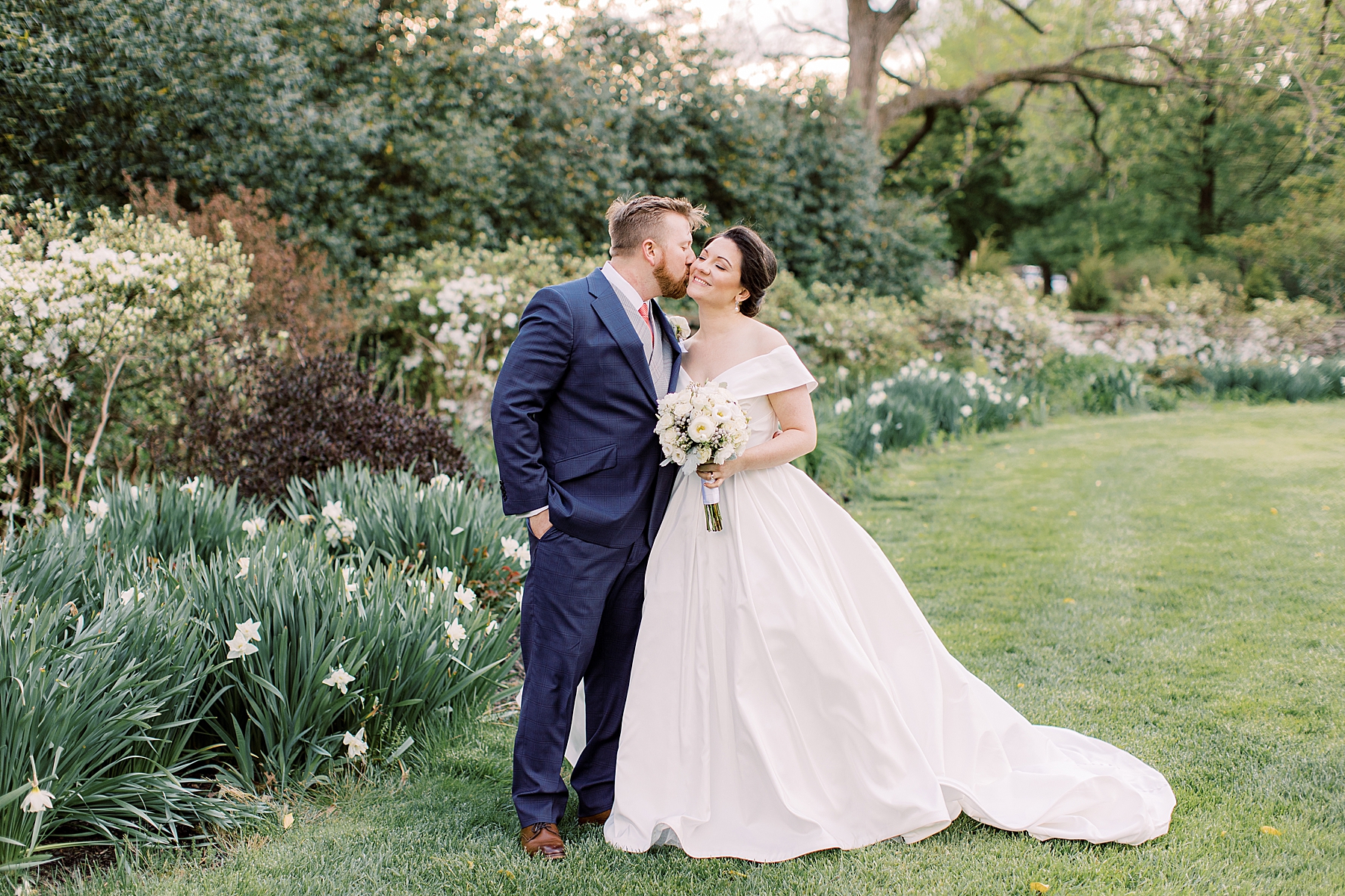 groom leans to kiss bride's cheek in garden at Bellevue Hall
