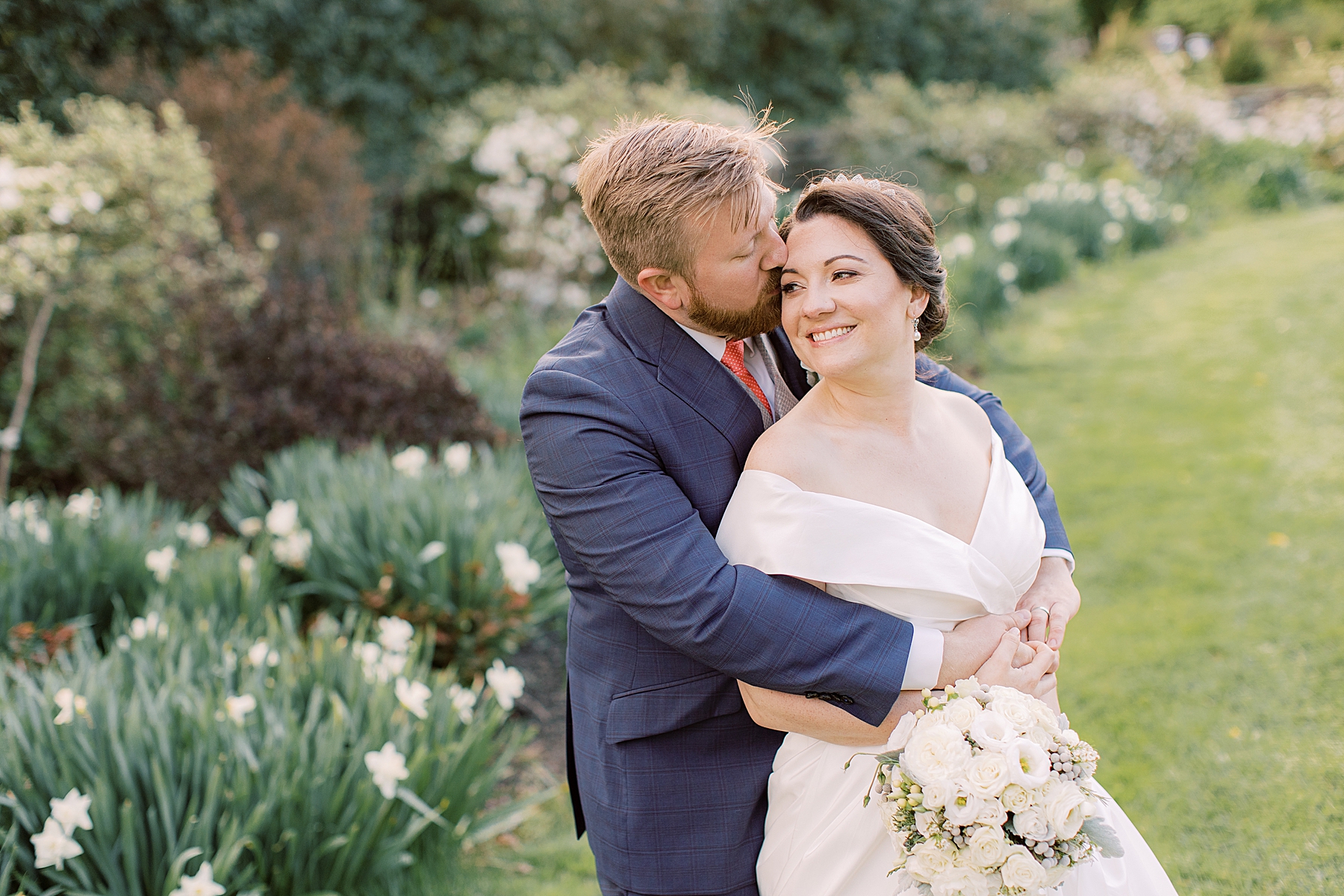 groom hugs bride from behind in front of daffodils 