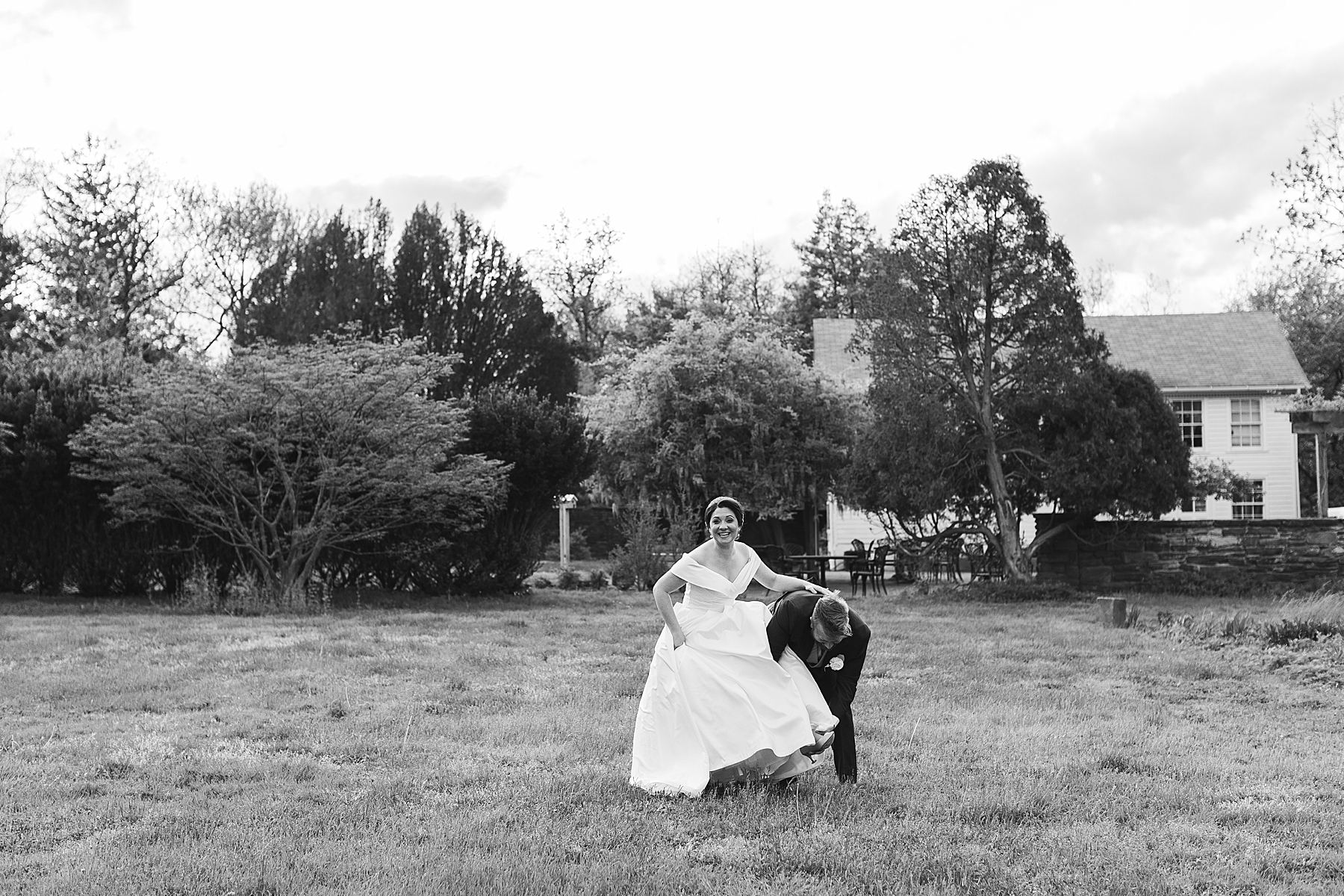 groom leans to help bride fix shoe on lawn at Bellevue Hall