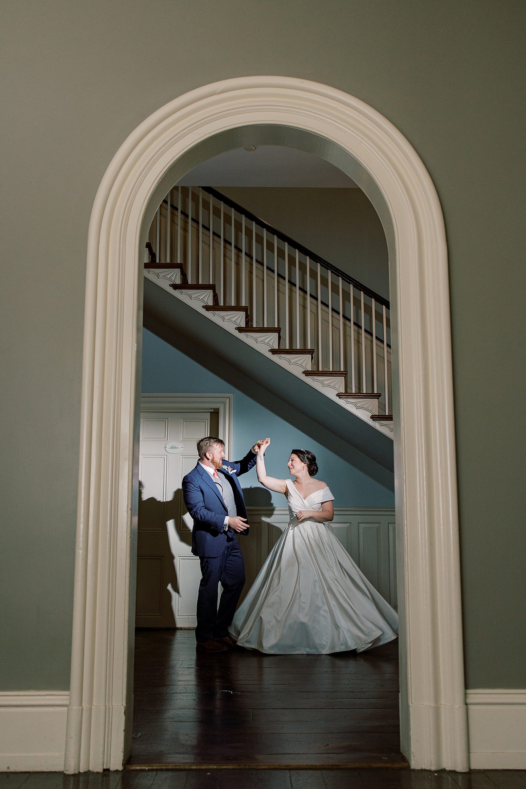 groom twirls bride under staircase inside Bellevue Hall 