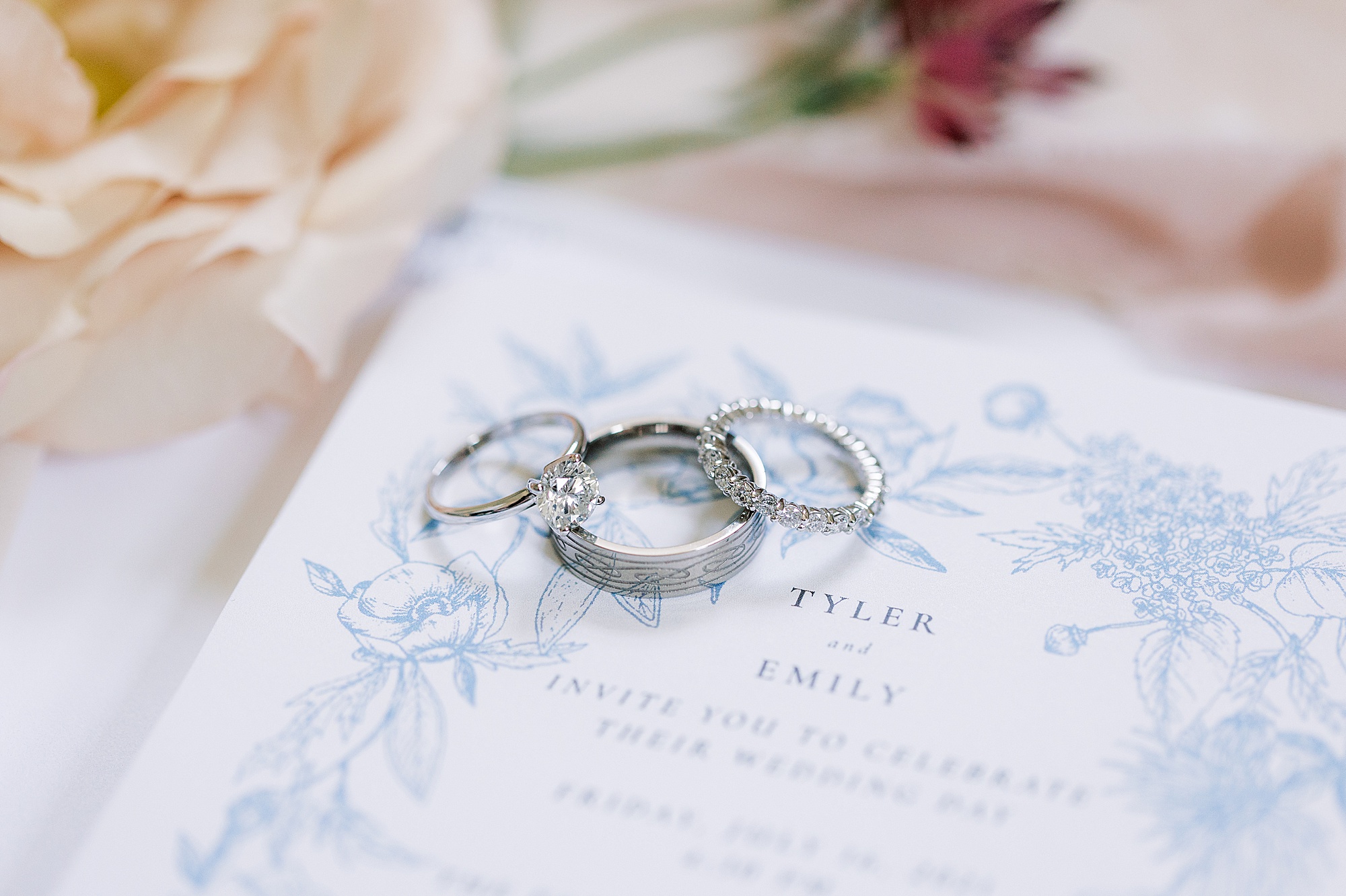 silver wedding bands lay stacked on blue and white invitation suite 