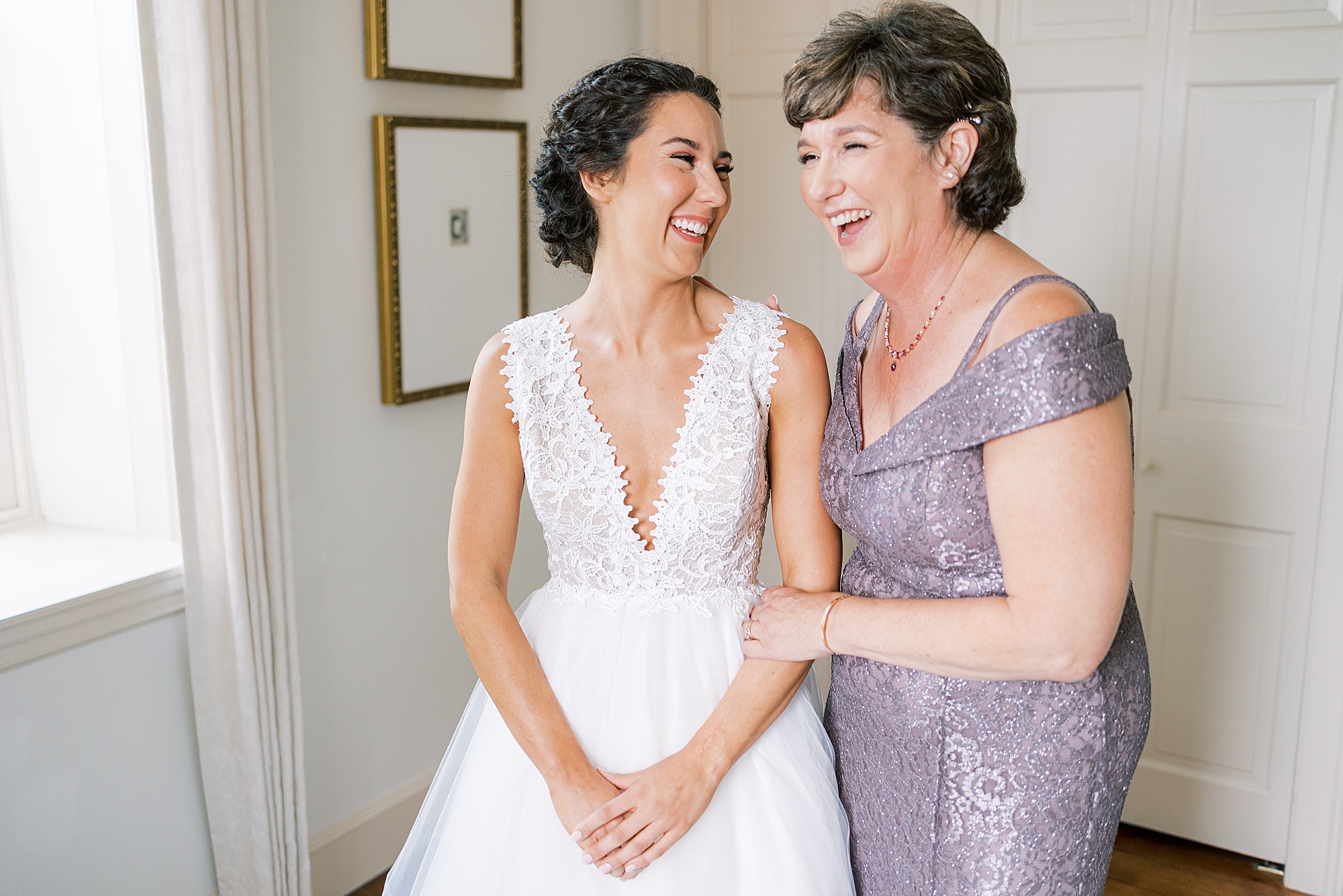bride and mother laugh together in room after wedding prep 