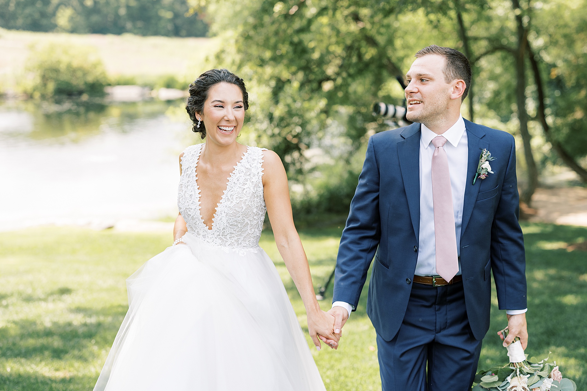 newlyweds smile and laugh walking together by creek