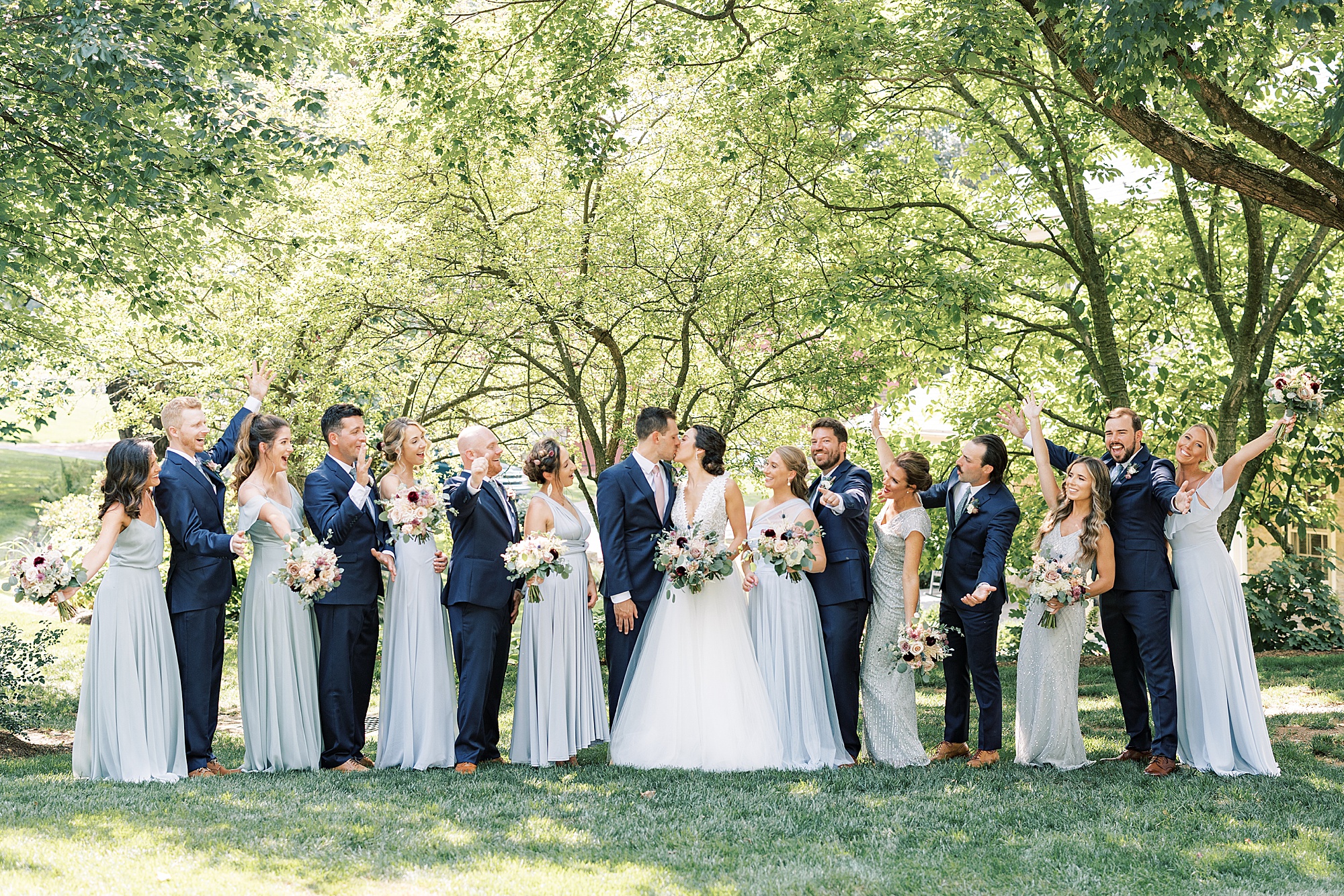 bride and groom kiss while wedding party in blue suits and mismatched blue gowns cheer 