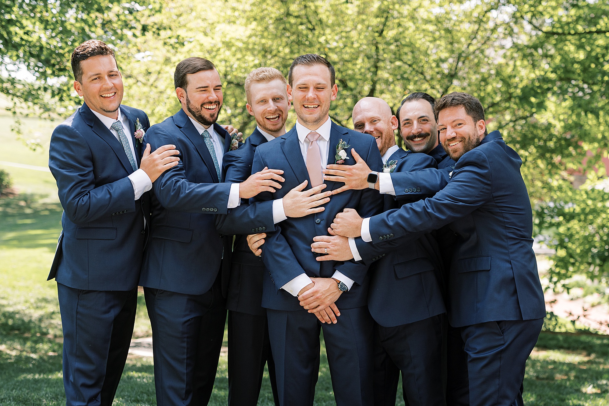 groomsmen hug groom from behind during summer wedding portraits 