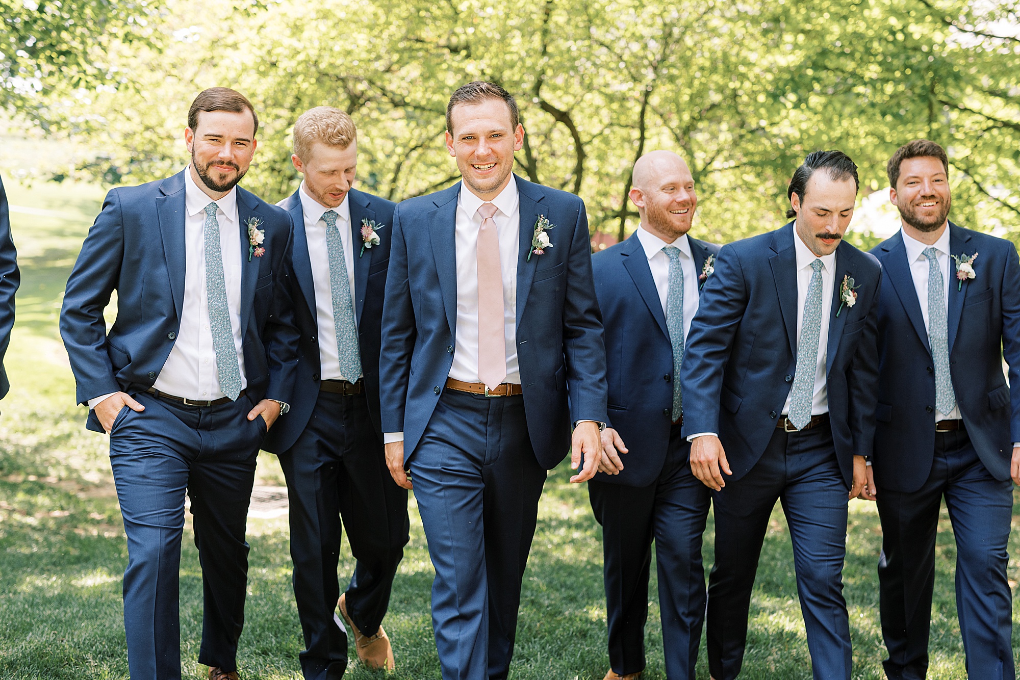 groom walks with groomsmen in blue suits on lawn 