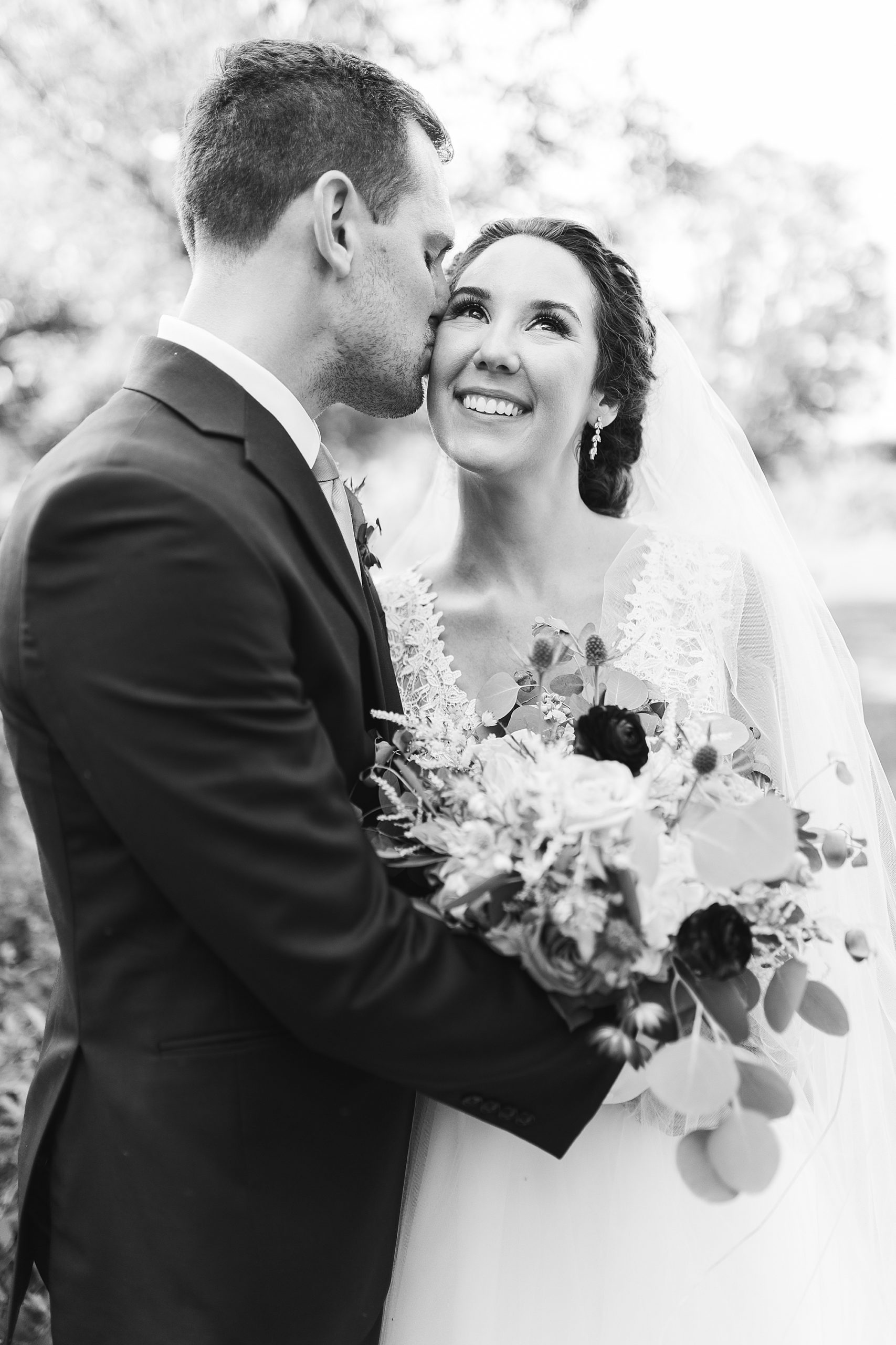 black and white portrait of groom kissing wife on cheek 